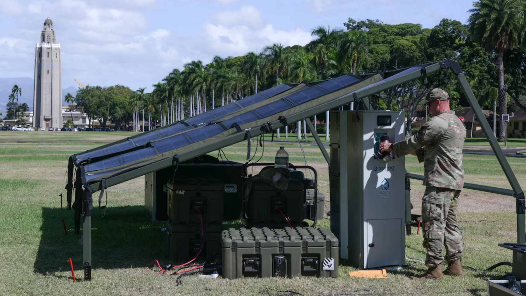 A U.S. Army soldier operating a mobile atmospheric water generator powered by a portable solar panel array in a field.