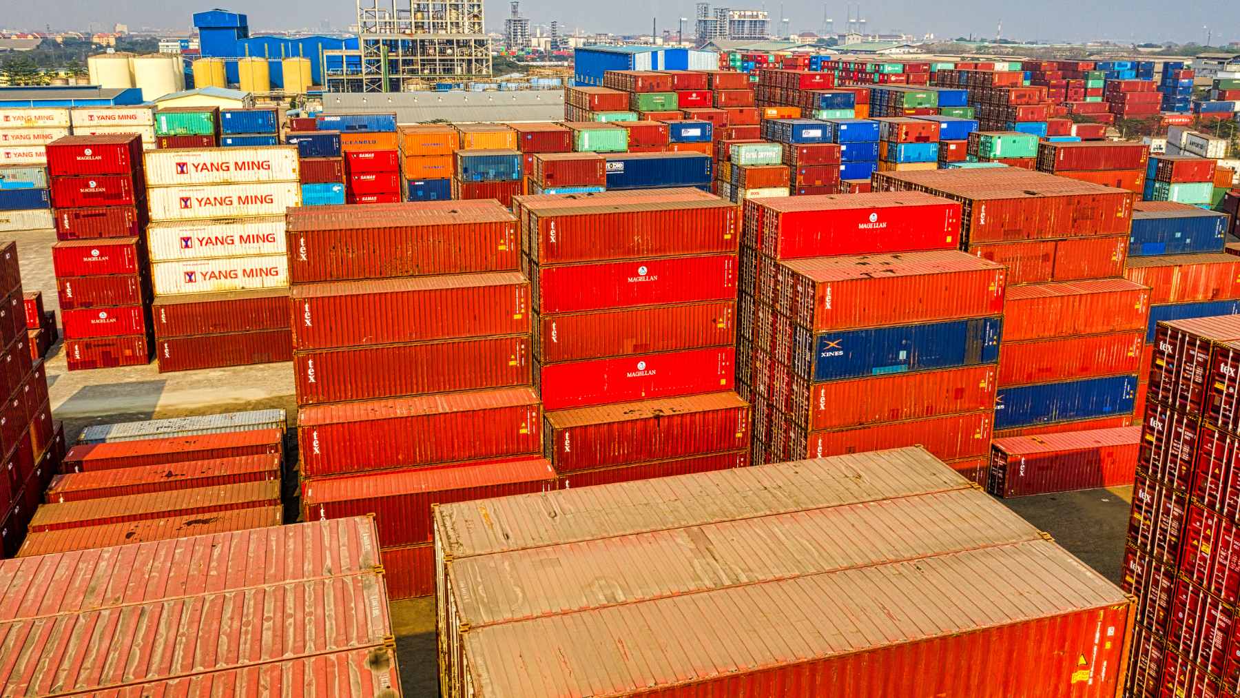 A digital illustration of the American and Indian flags flanking a shipping container and oil barrels, symbolizing the 2026 trade and energy agreement.