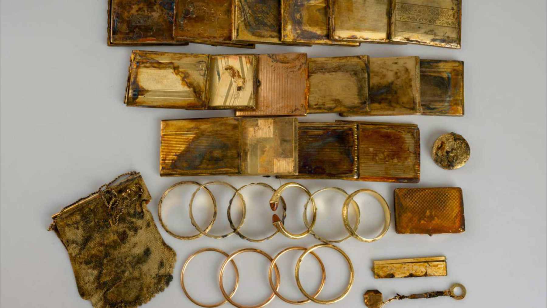 A weathered, plain aluminum can partially exposed in a mossy stone wall, revealing a stash of shining gold coins inside.