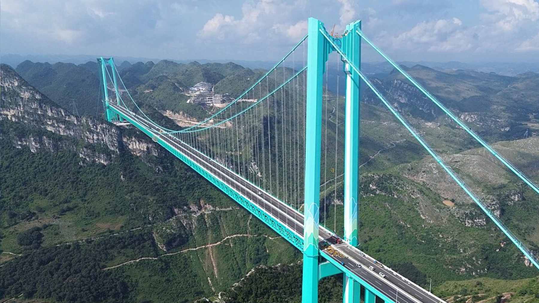 A massive suspension bridge spanning a deep, misty canyon, featuring an artificial waterfall cascading from its structure.