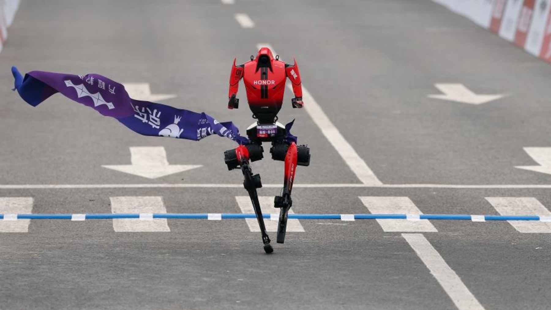 An advanced autonomous humanoid robot running on a paved city street during a half-marathon race.