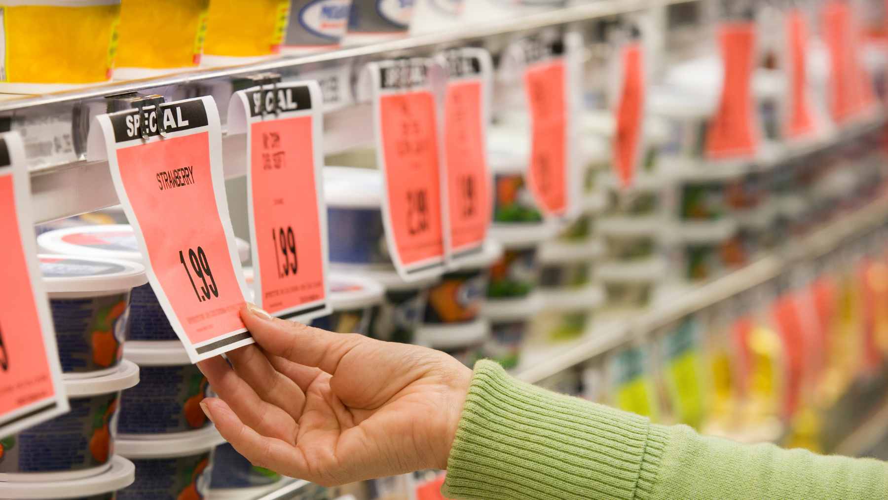 A close-up of a digital electronic price tag on a grocery store shelf next to fresh produce.