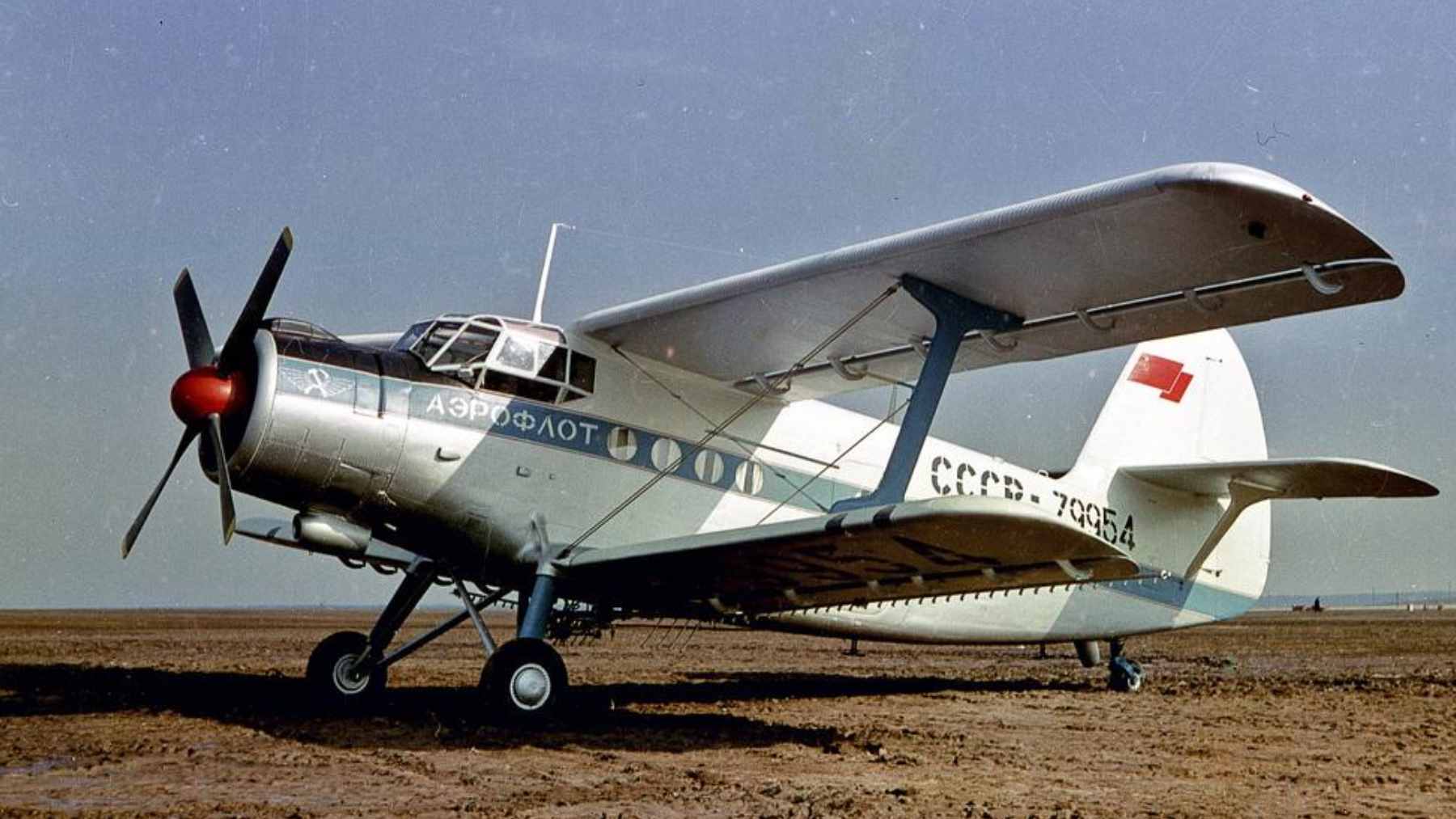 An aging Soviet-era Antonov An-2 biplane parked on a rural grassy airfield.
