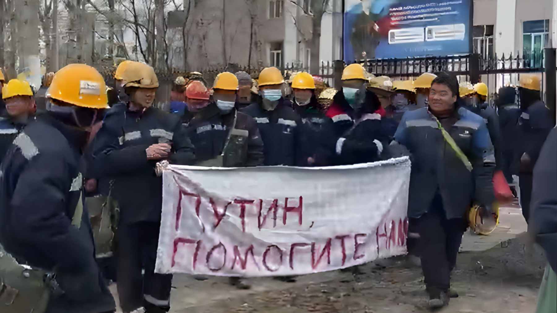 A large crowd of Chinese workers protesting with signs on a street near an industrial refinery site in Russia.