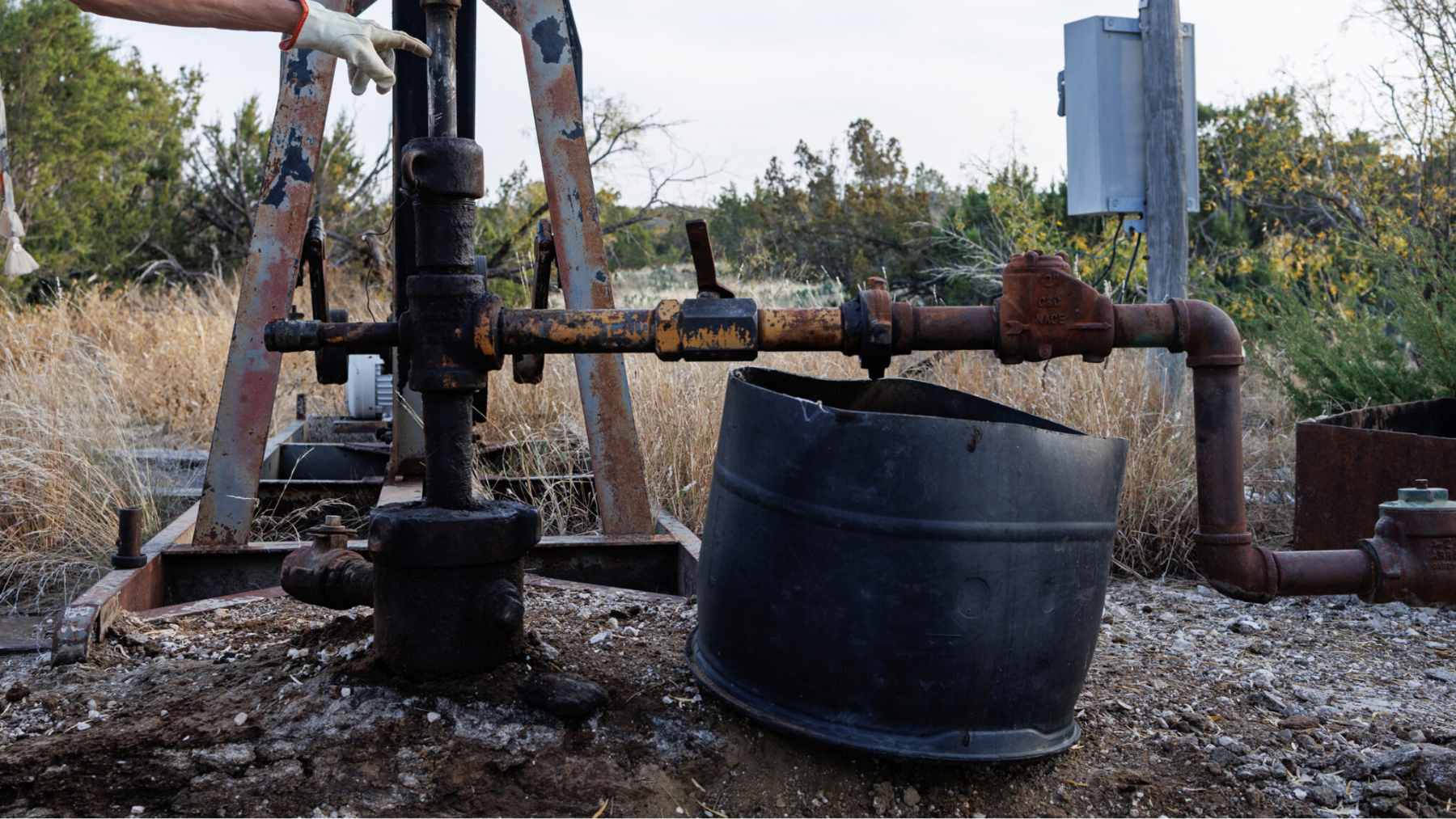 An old, rusted oil pumpjack sitting in a Texas field with visible signs of leakage around the base.