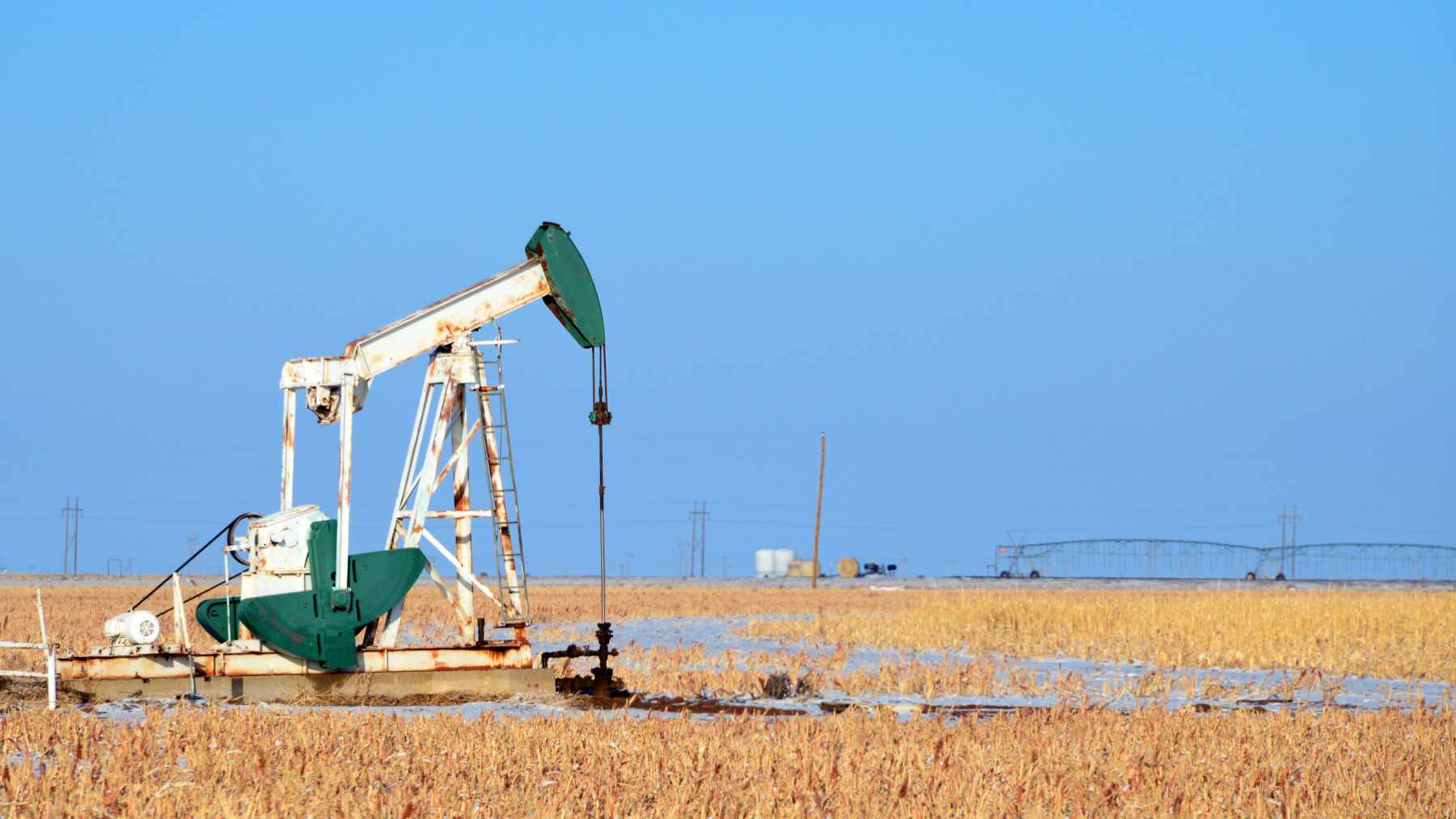 An old, rusted oil pumpjack sitting in a Texas field with visible signs of leakage around the base.