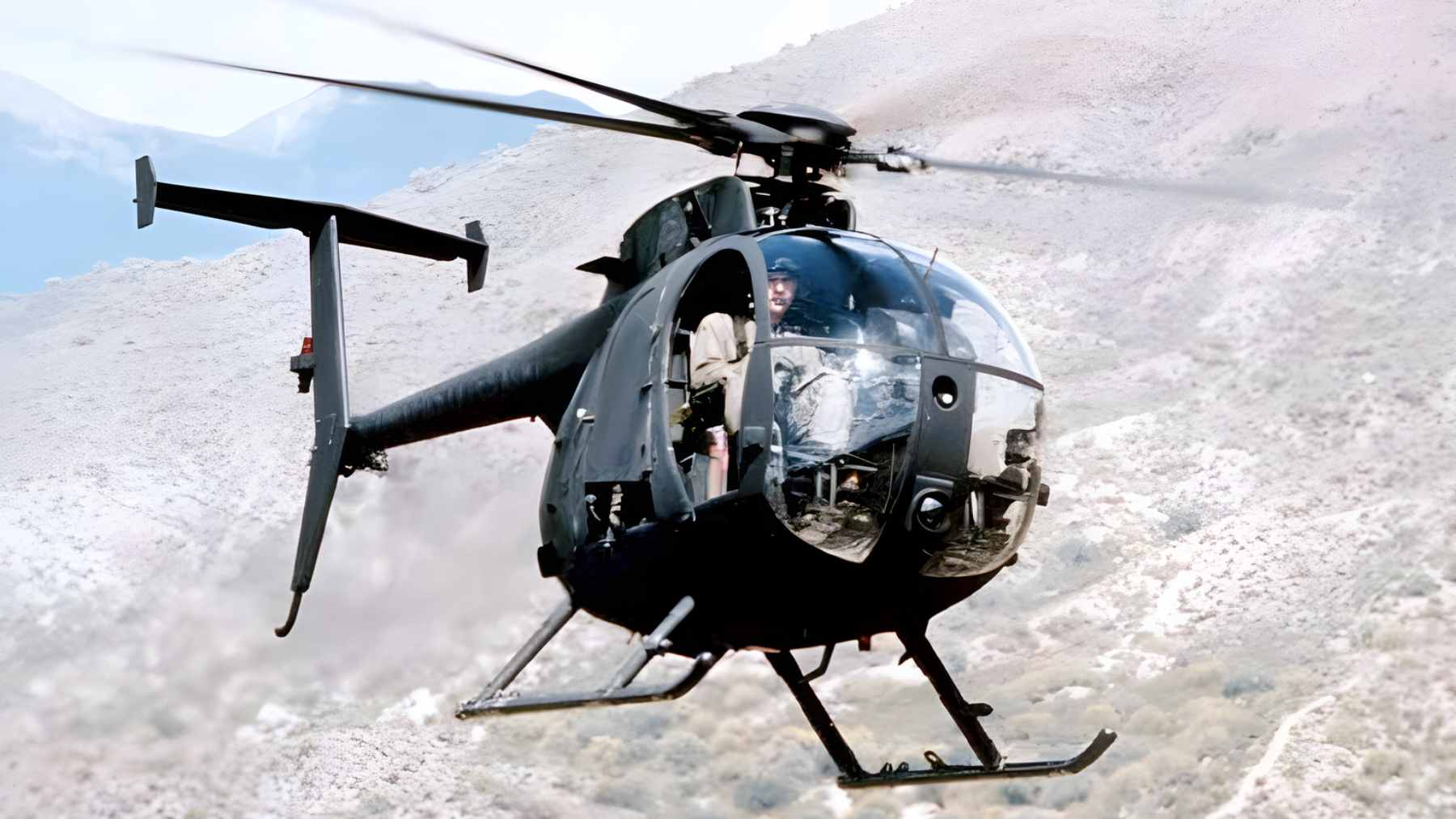 A U.S. military MH-6 Little Bird helicopter operating in a muddy, austere environment.