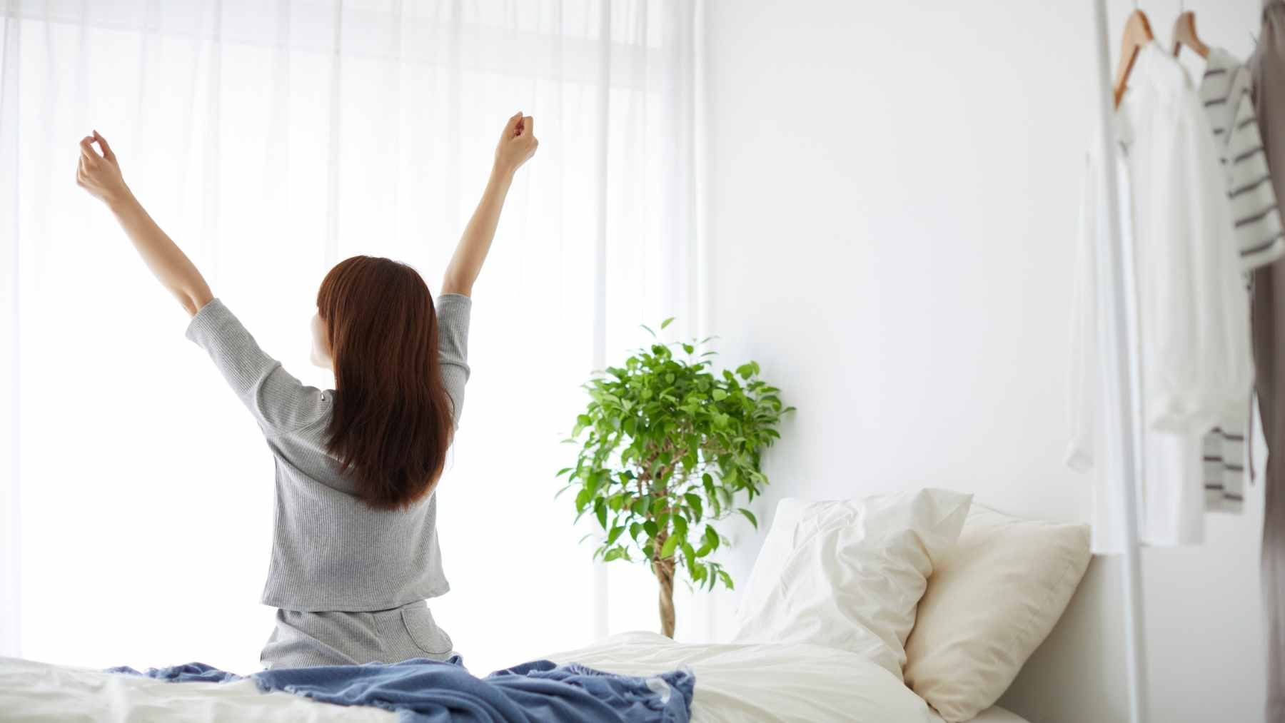 A person waking up in bed as bright morning sunlight streams through the bedroom window.