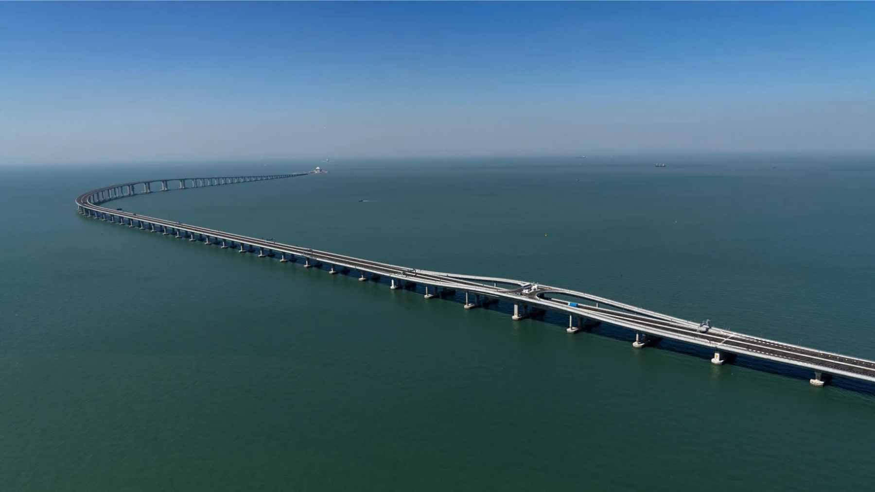 An aerial view of the Hong Kong–Zhuhai–Macao Bridge stretching across the Pearl River Delta, showing the transition between bridge spans and artificial islands.