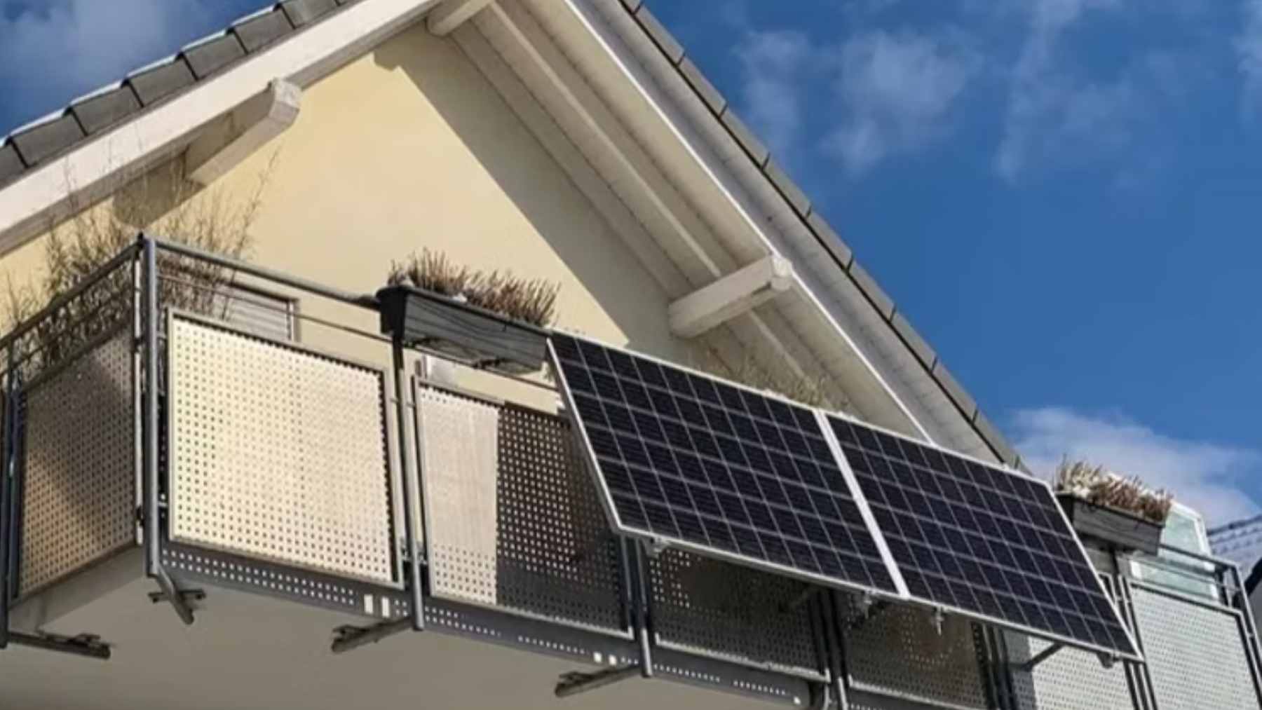 Small solar photovoltaic panels mounted to an apartment balcony railing in an urban housing complex.