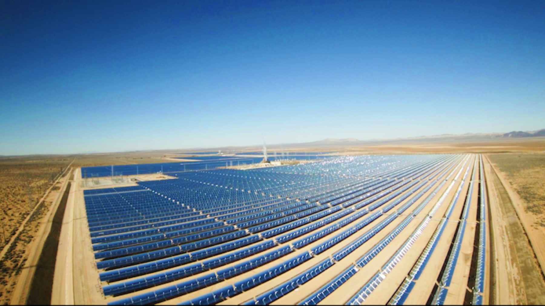 Aerial view of the Ivanpah Solar Electric Generating System in the Mojave Desert, showing rows of heliostat mirrors surrounding a central tower.