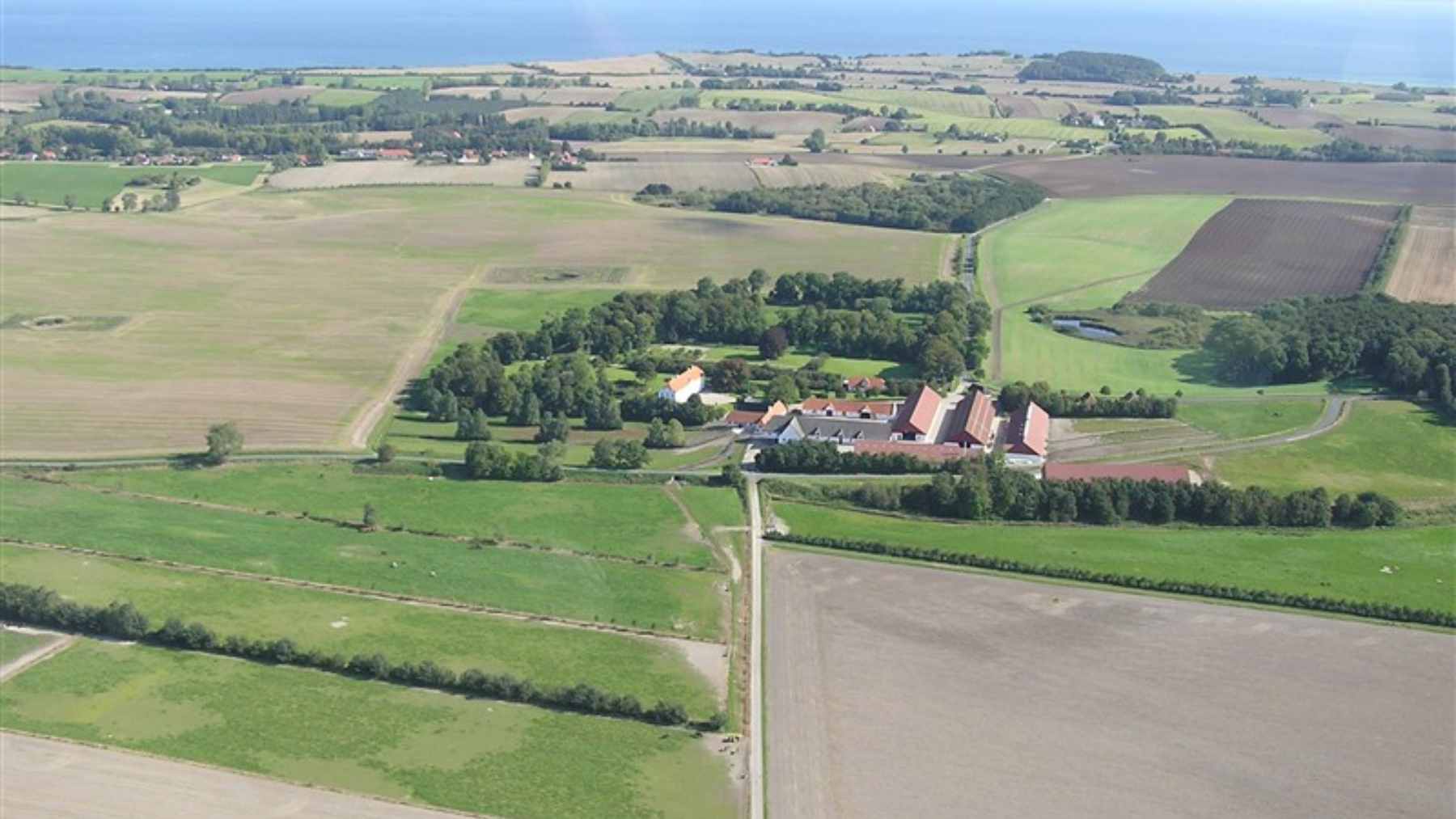 Lush green agricultural fields and traditional farm buildings of the Schelenborg Gods estate on the island of Funen, Denmark.