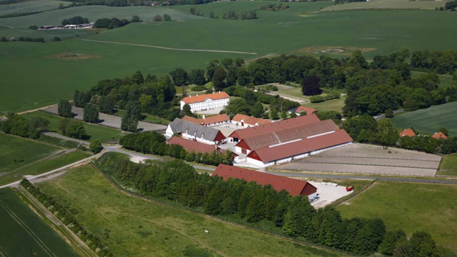 Lush green agricultural fields and traditional farm buildings of the Schelenborg Gods estate on the island of Funen, Denmark.