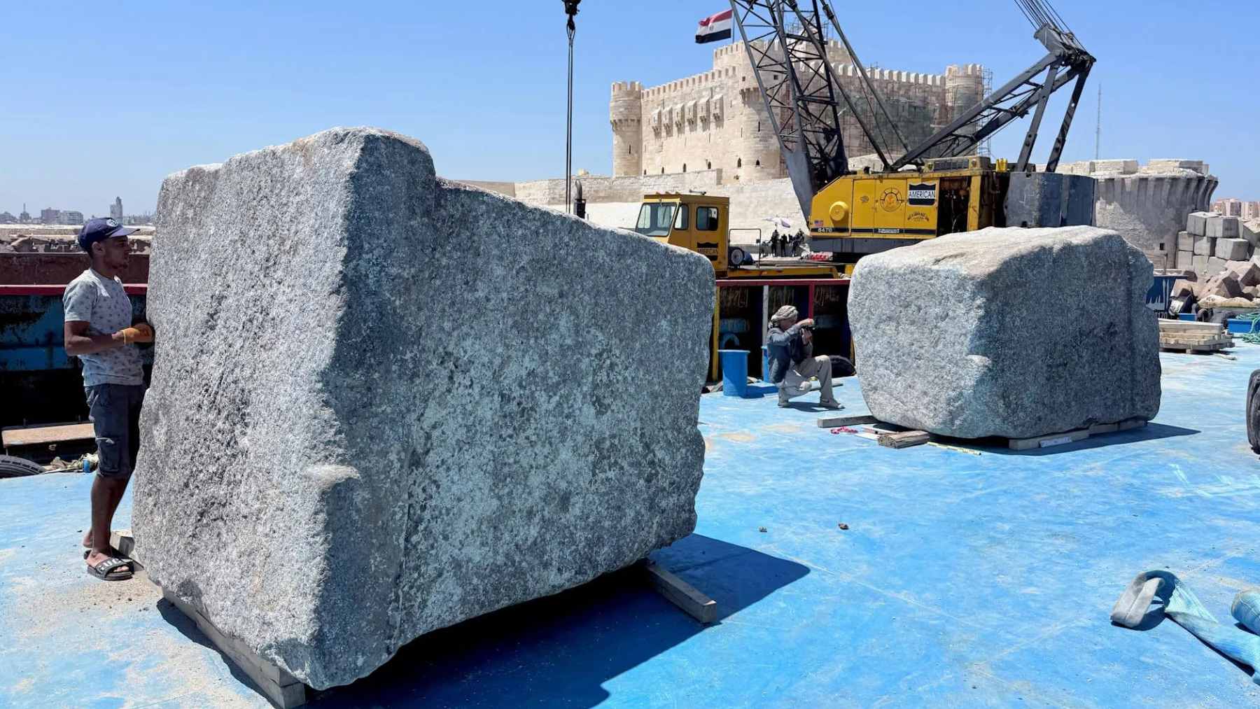 Massive granite blocks from the Lighthouse of Alexandria being lifted from the Mediterranean Sea by a crane.