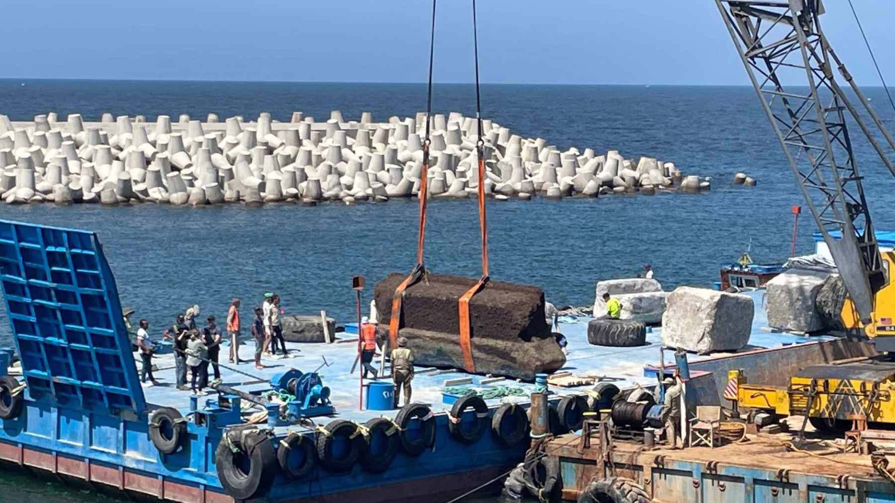 Massive granite blocks from the Lighthouse of Alexandria being lifted from the Mediterranean Sea by a crane.