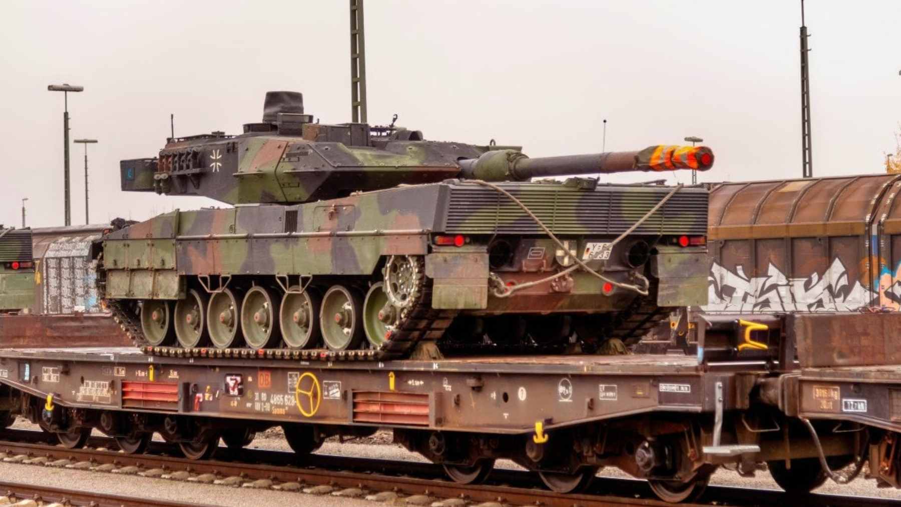 A European freight train loaded with NATO military vehicles and heavy equipment moving through a transit route.