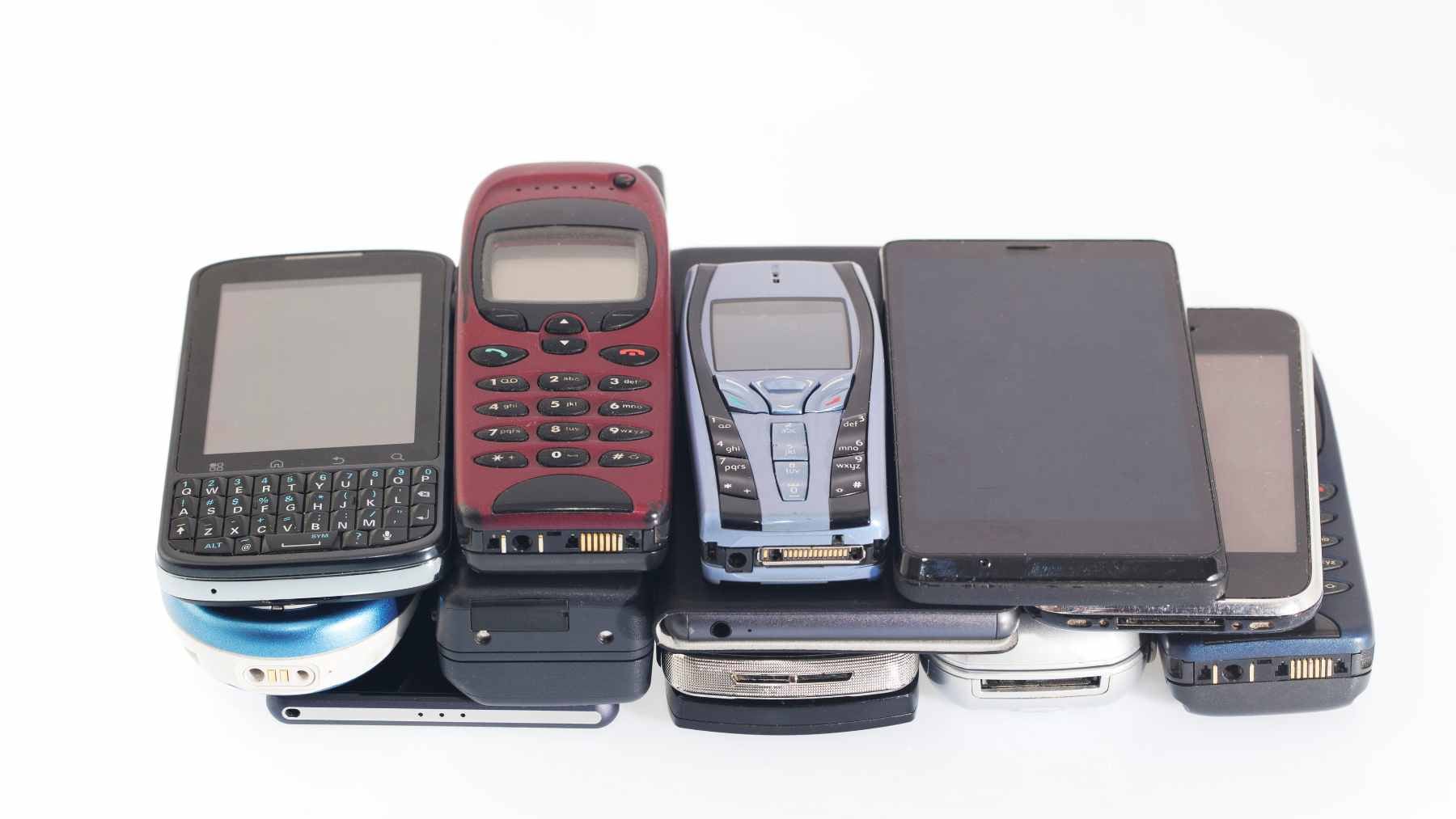 A collection of used iPhones and Samsung Galaxy smartphones piled inside a wooden storage drawer.