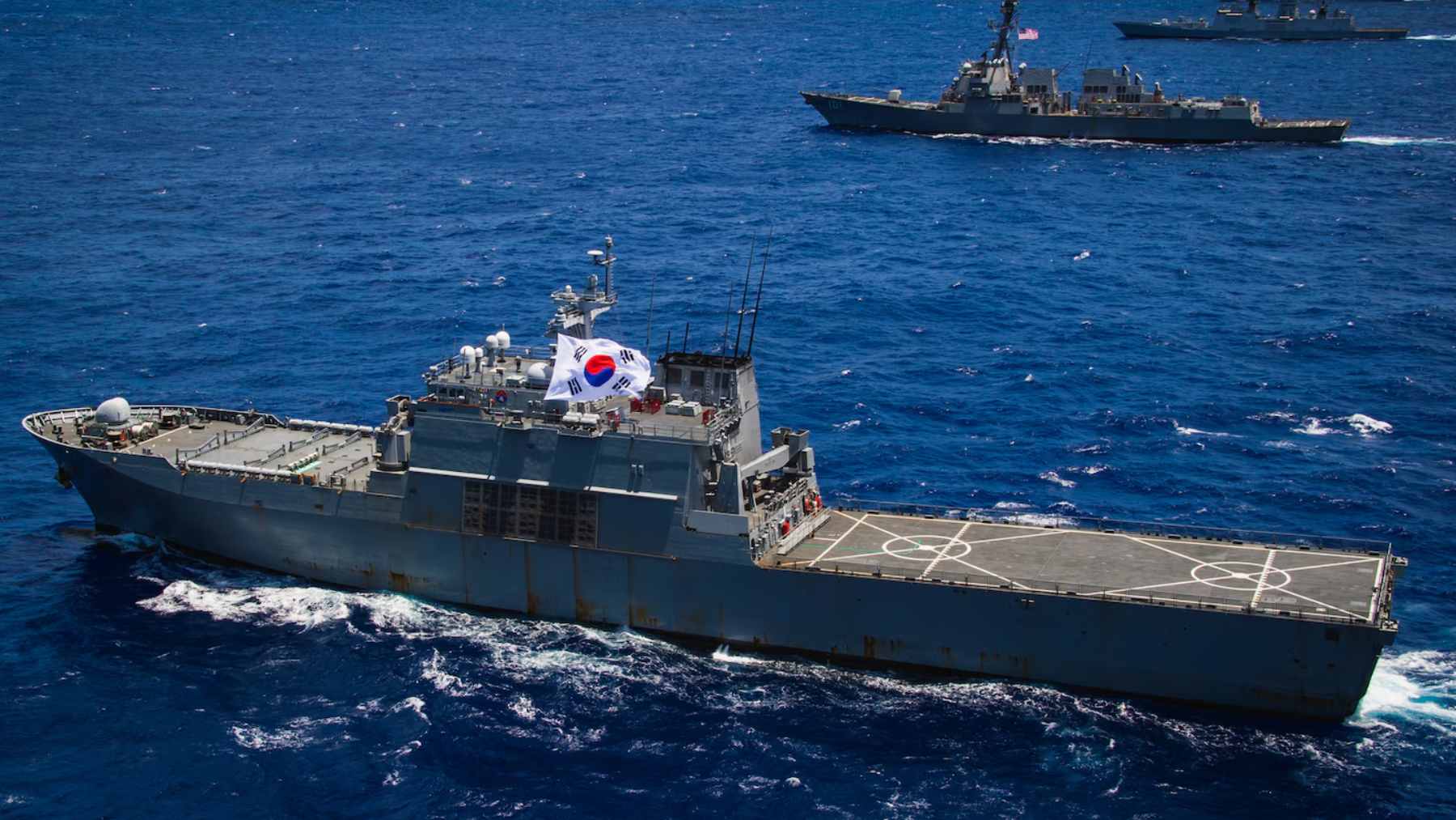 A high-angle view of a multinational naval fleet sailing in formation during RIMPAC maneuvers in the Pacific Ocean.