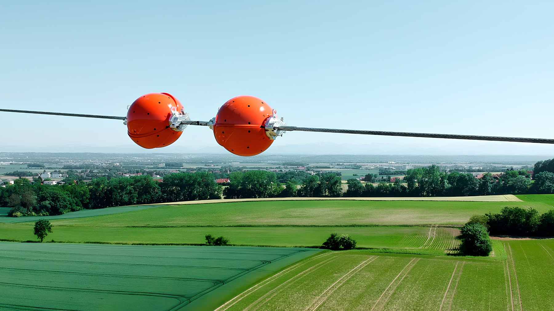 Bright aviation orange marker balls hanging from high-voltage transmission lines to increase visibility for low-flying aircraft.