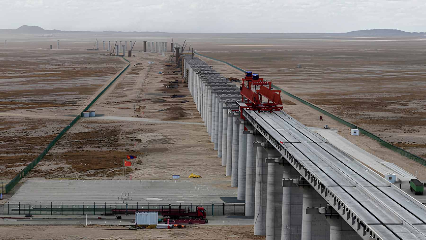 Heavy construction machinery installing massive concrete T-beams for the new Ganqimaodu to Gashuun Sukhait railway bridge in the Gobi Desert.