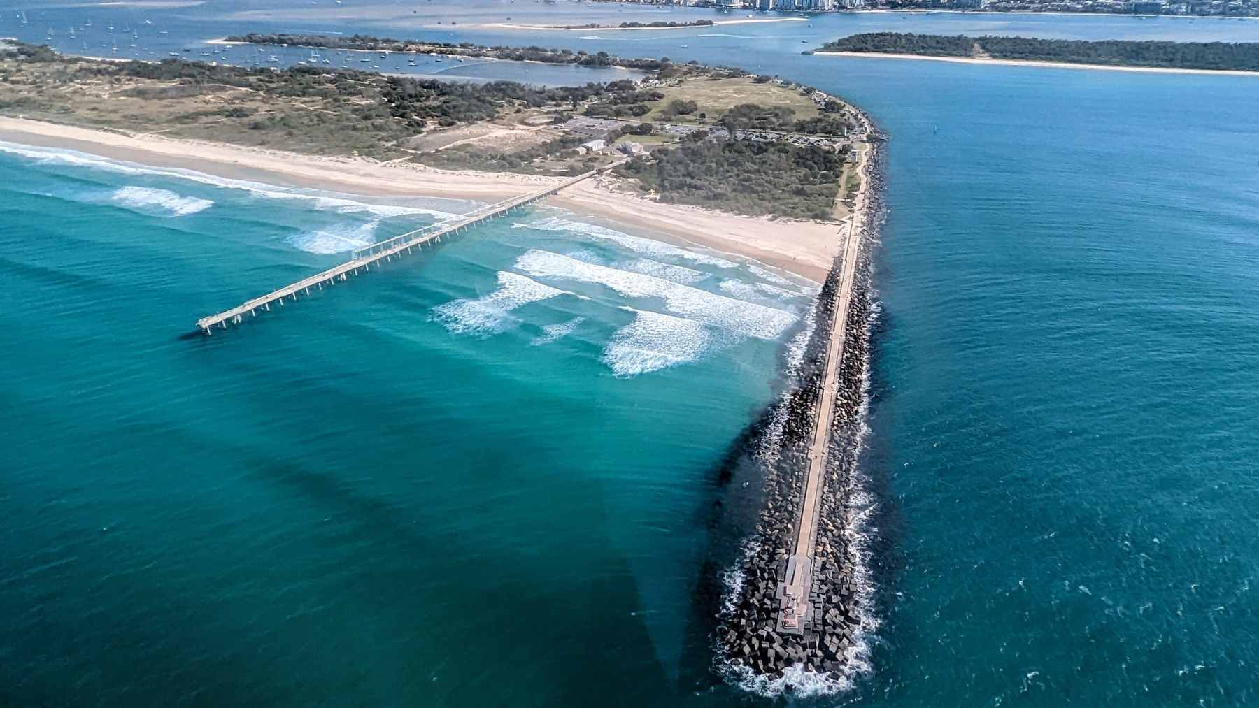 The Gold Coast Sand Bypass jetty extending into the Pacific Ocean, where submerged pumps move sand to prevent erosion and maintain navigation channels.