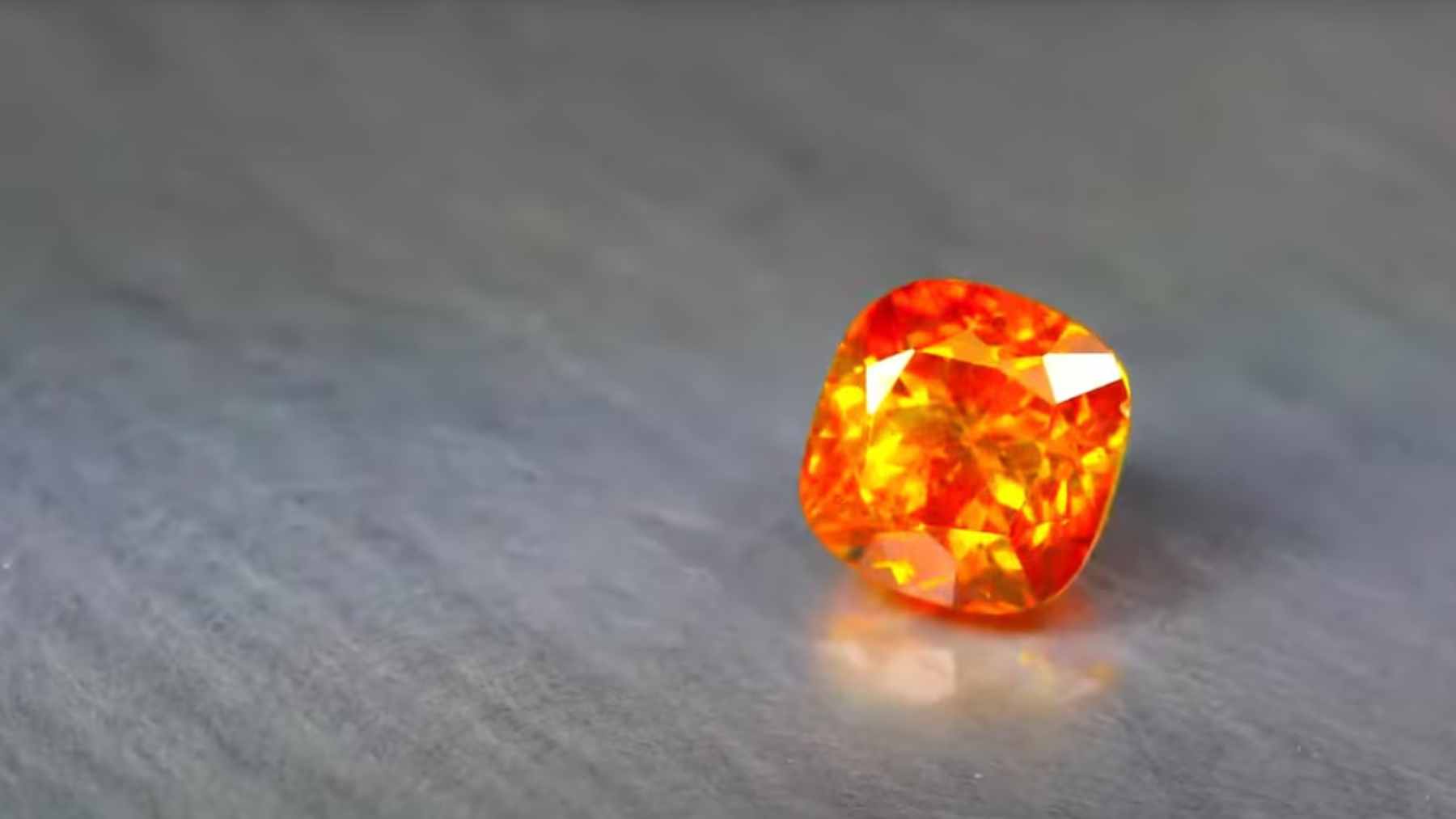 A high-resolution close-up of a tiny, reddish-orange kyawthuite crystal, highlighting its adamantine luster and unique structure.