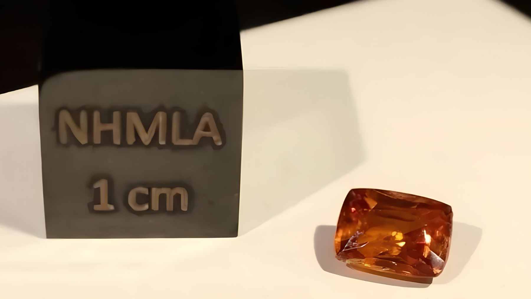 A high-resolution close-up of a tiny, reddish-orange kyawthuite crystal, highlighting its adamantine luster and unique structure.