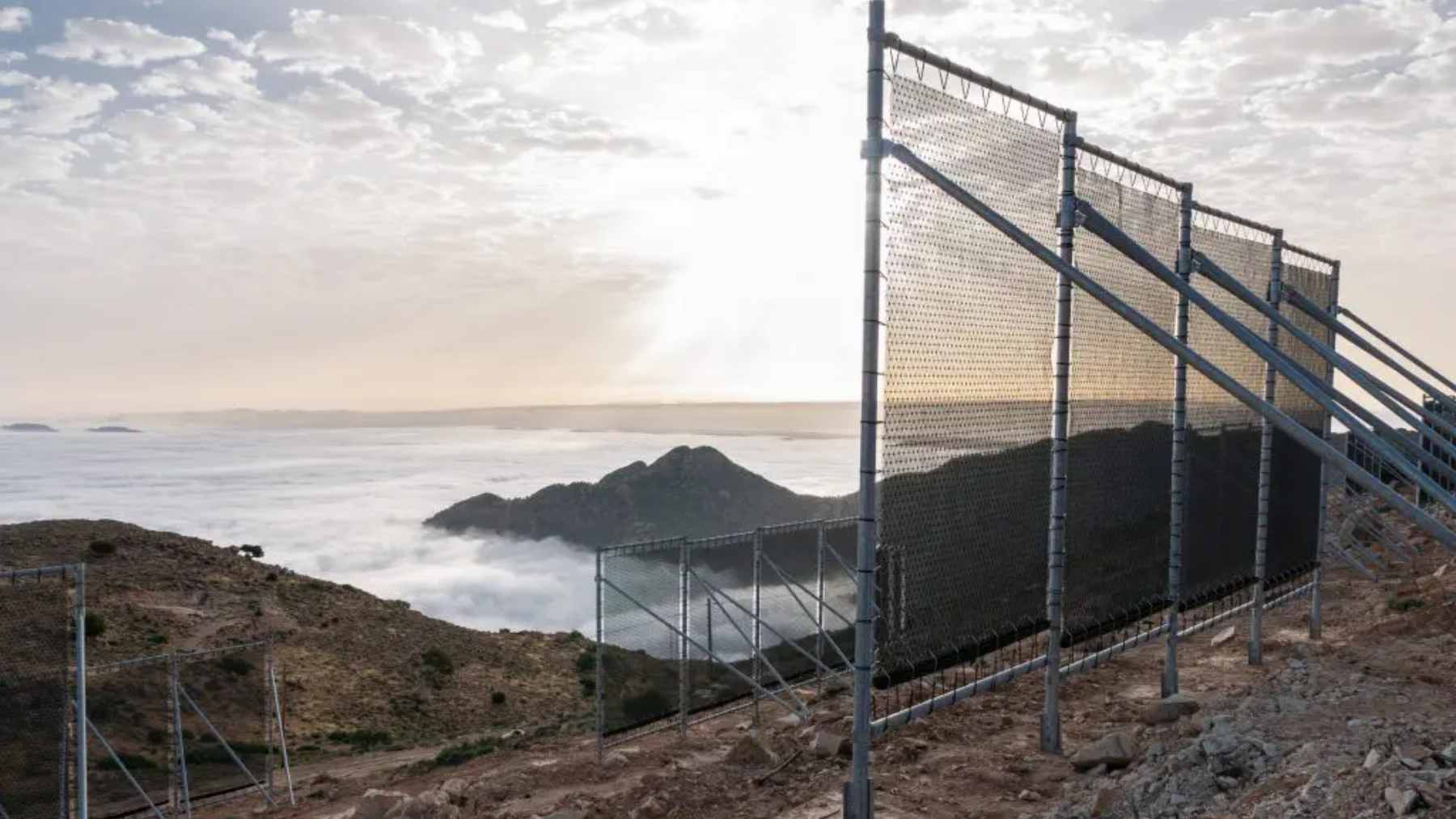 A wide view of large, mesh fog-collection nets installed on the ridge of Mount Boutmezguida in Morocco to capture mountain mist for drinking water.