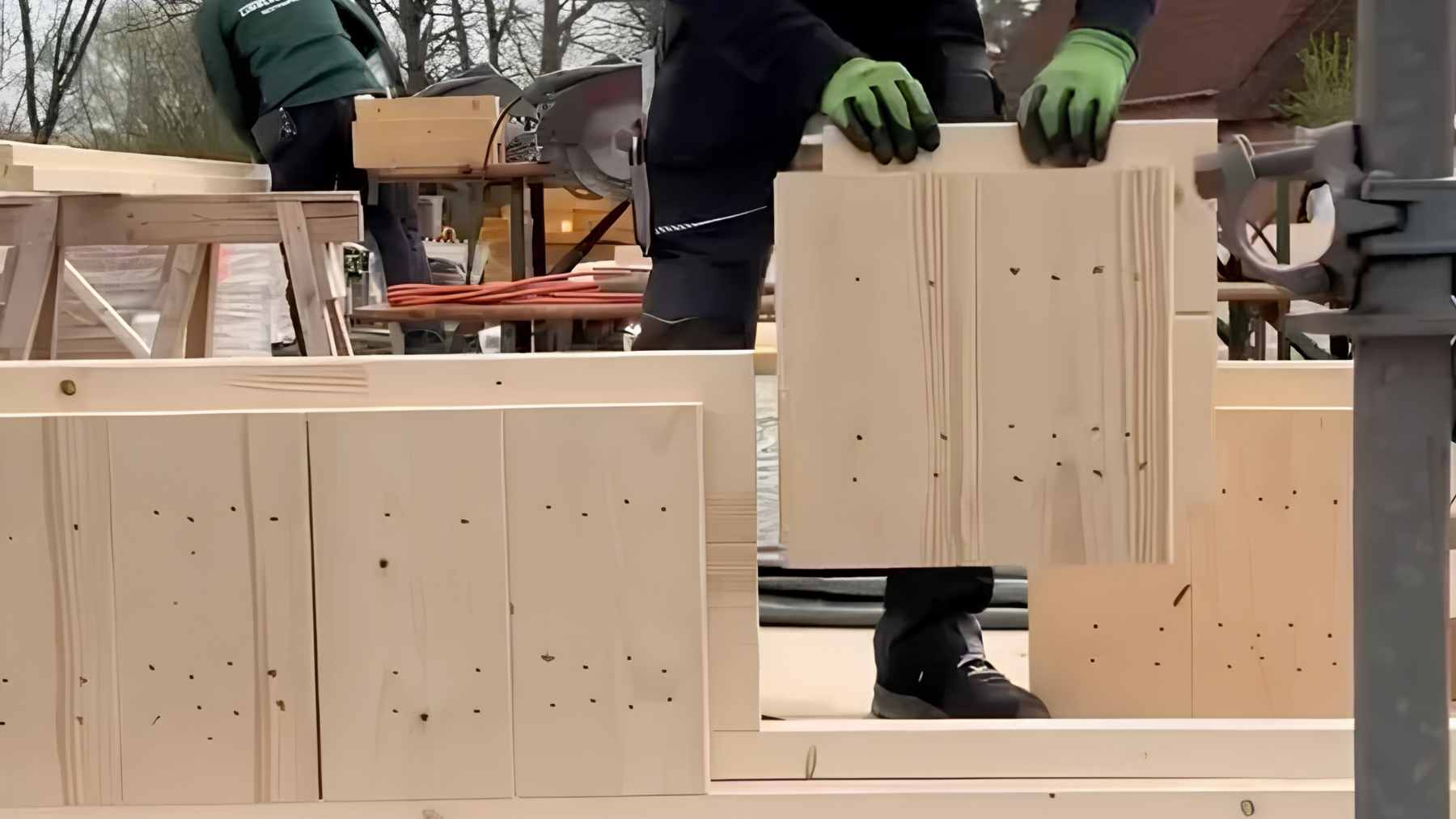 A construction crew assembling the structural walls of a house using large, interlocking solid-wood blocks that require no mortar or glue.