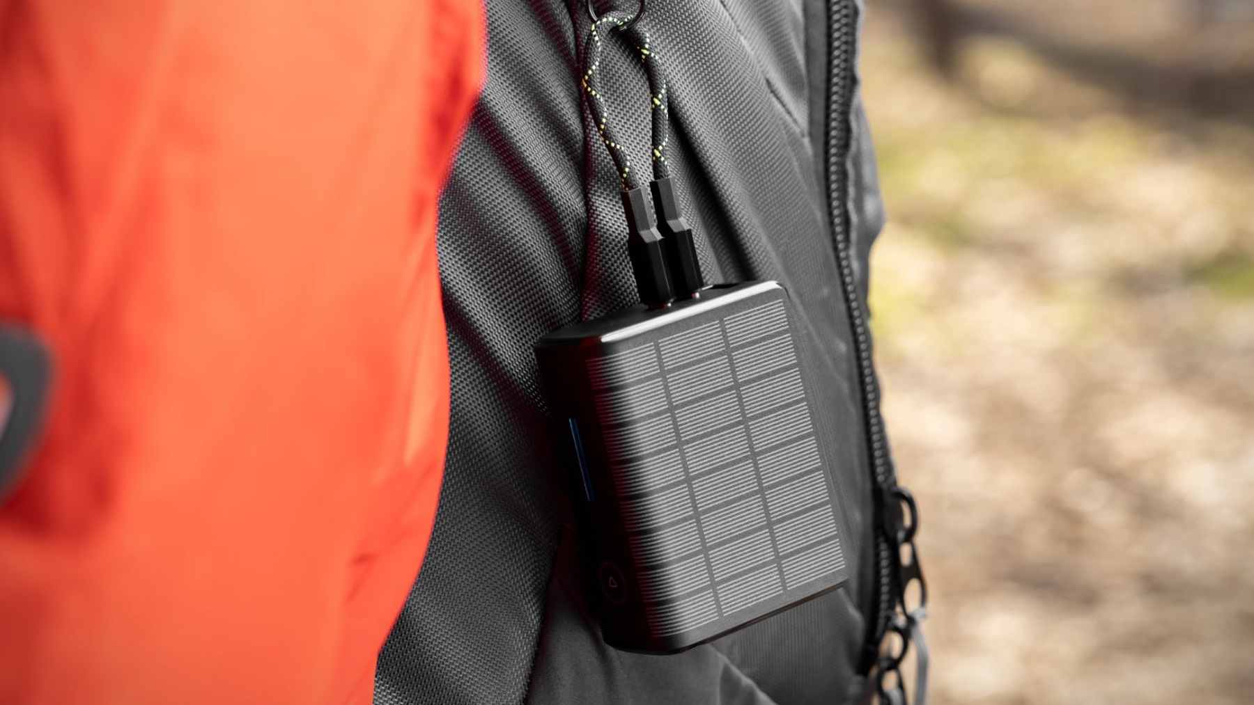 A compact Solly solar power bank shown next to a laptop and smartphone, highlighting its multiple ports and integrated wall plug.