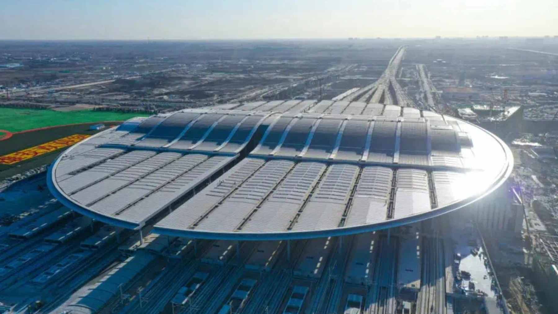 An aerial view of the oval-shaped Xiong’an Railway Station, showcasing its massive scale and solar panel-covered roof.