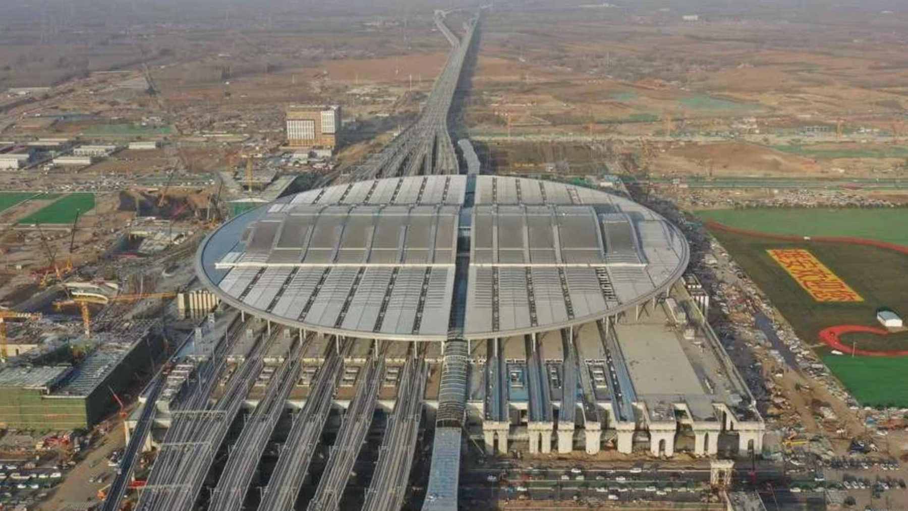China built Asia’s largest rail station in two years, with 5.1 million ft.² and welding robots setting the pace 1 Aerial view of the oval-shaped Xiong’an Railway Station, showcasing its massive roof integrated with solar panels.