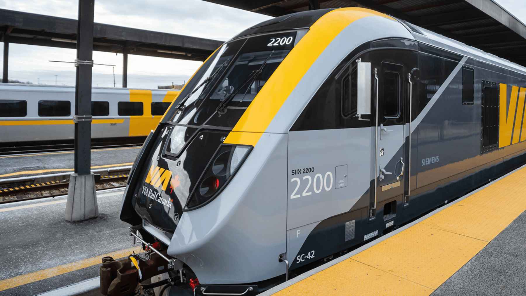 A passenger train railcar undergoing mechanical overhaul at a maintenance facility, representing CAD Railway Industries' refurbishment project for VIA Rail sleeper cars.