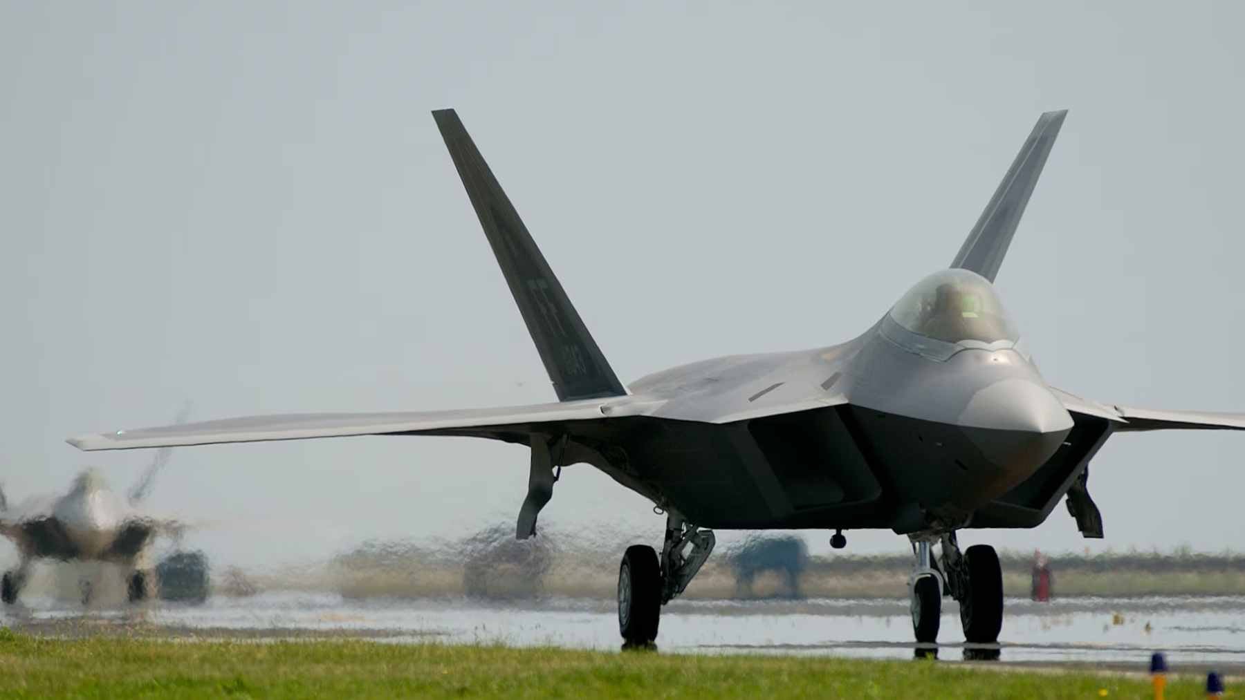 A technician reviewing digital diagnostic data on a laptop while working on an F119 turbofan engine of an F-22 Raptor.