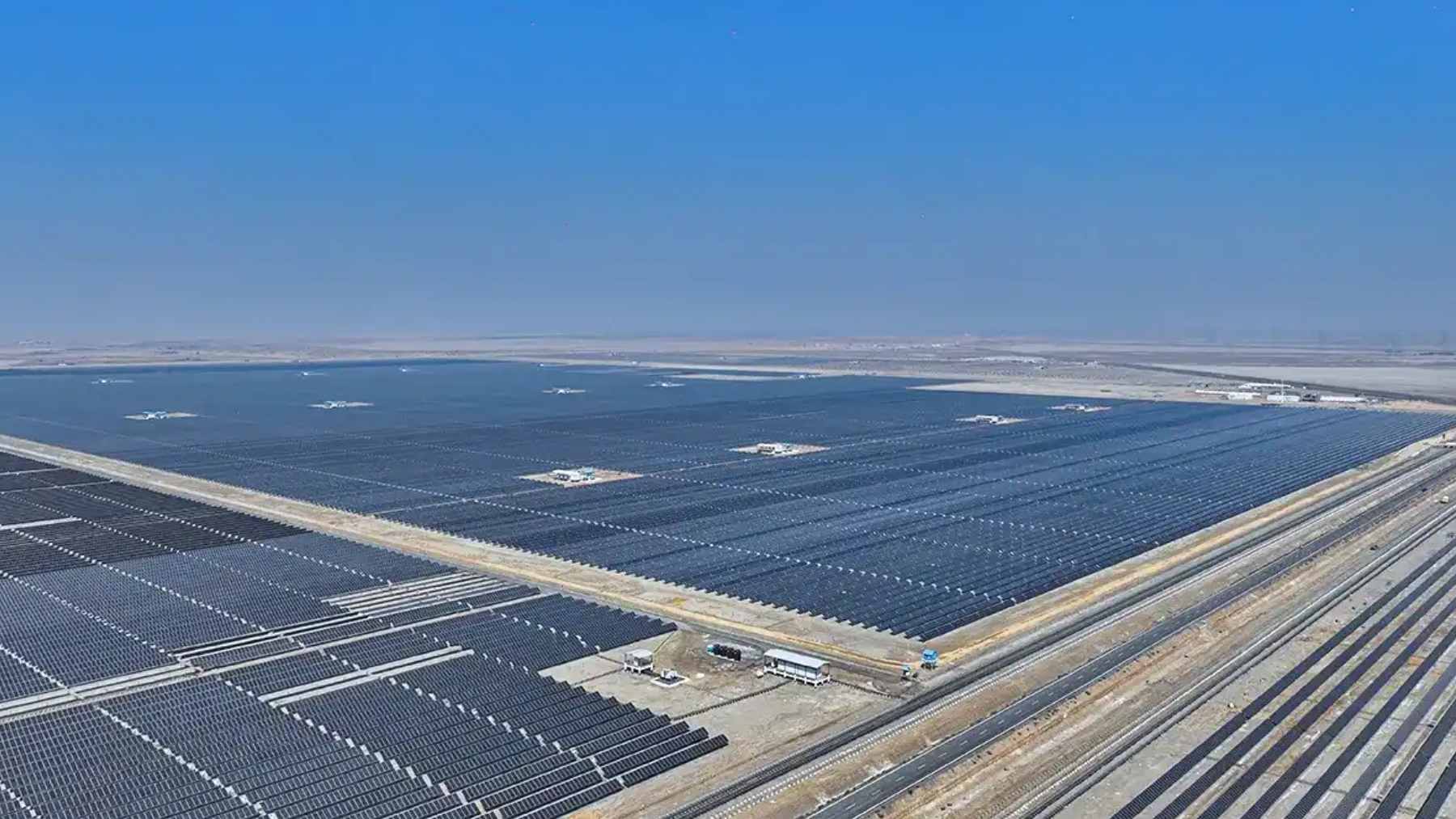 Rows of bifacial solar panels and wind turbines stretching across the arid salt flats of the Khavda Renewable Energy Park in Gujarat, India.