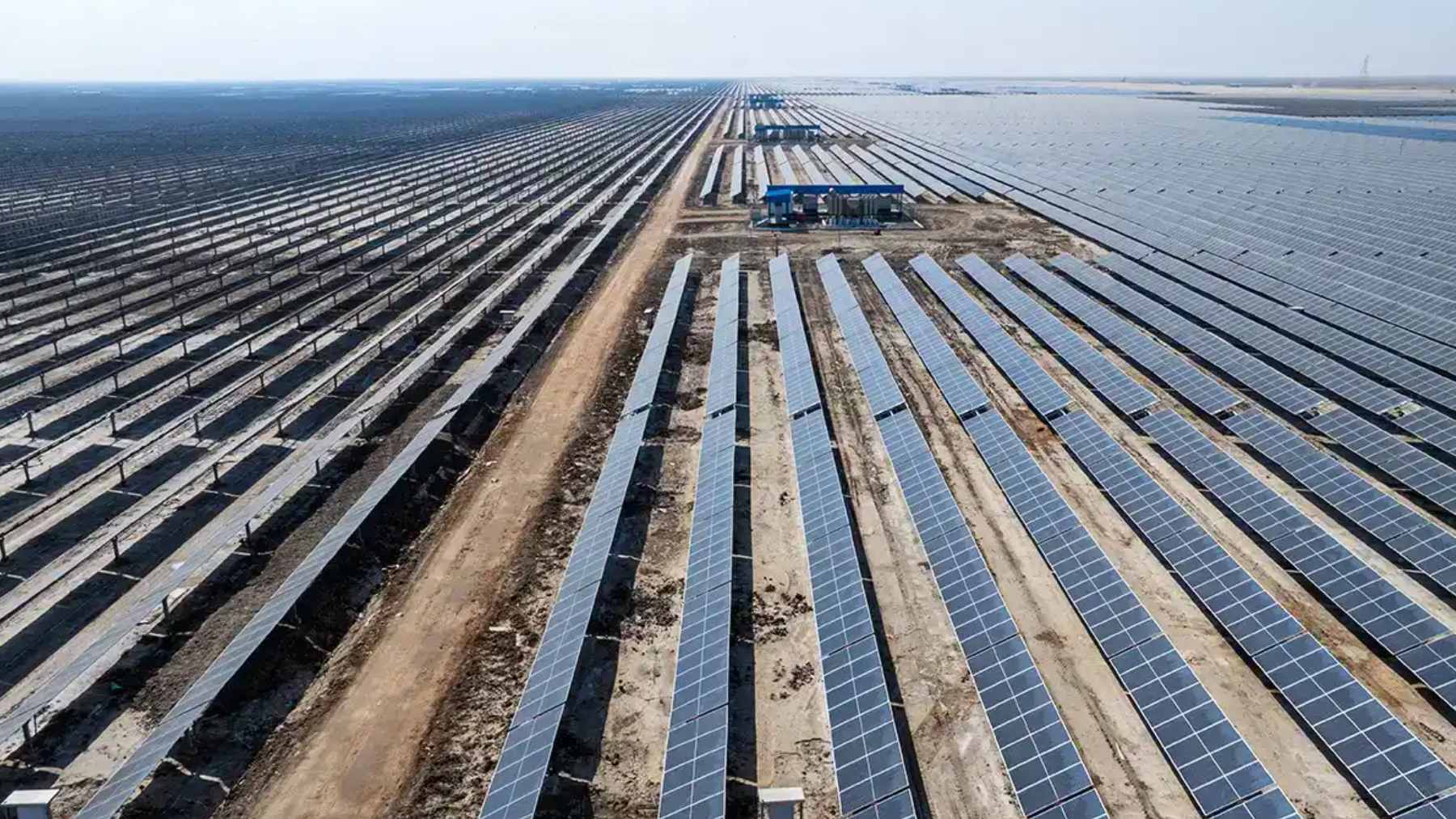 Rows of bifacial solar panels and wind turbines stretching across the arid salt flats of the Khavda Renewable Energy Park in Gujarat, India.