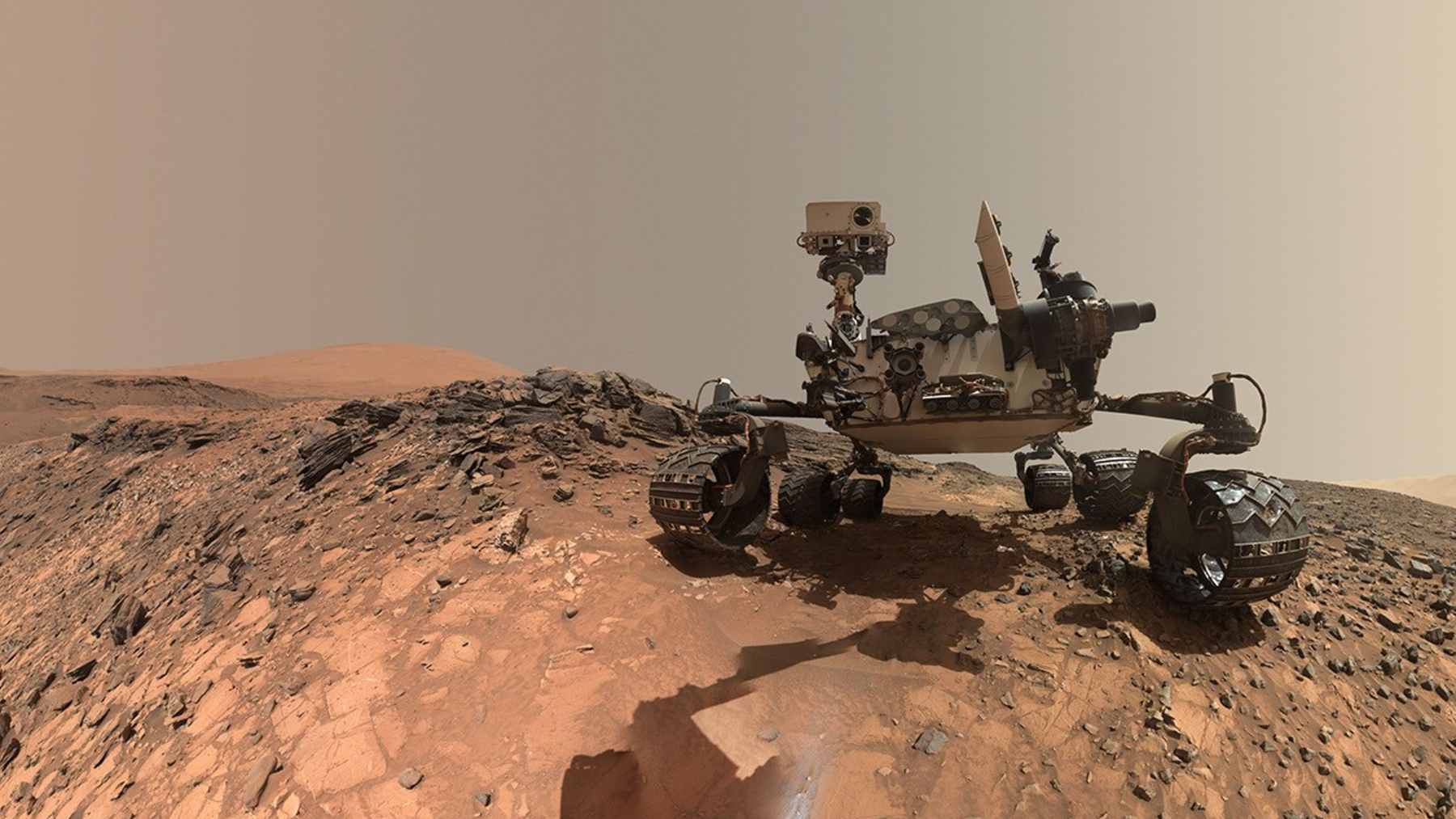The NASA Curiosity rover traversing the rugged Martian terrain of Gale Crater while climbing Mount Sharp.