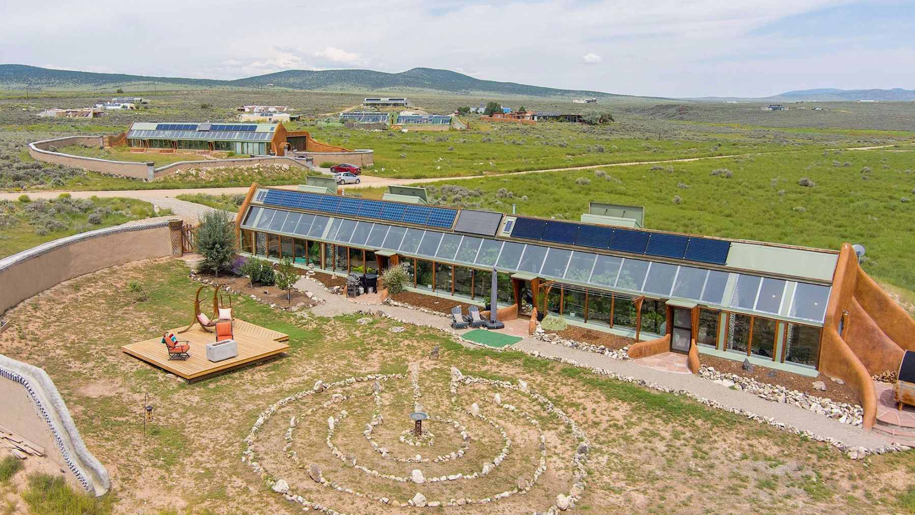 A natural swimming pond surrounded by desert landscaping in a New Mexico Earthship community, featuring native plants for water filtration.
