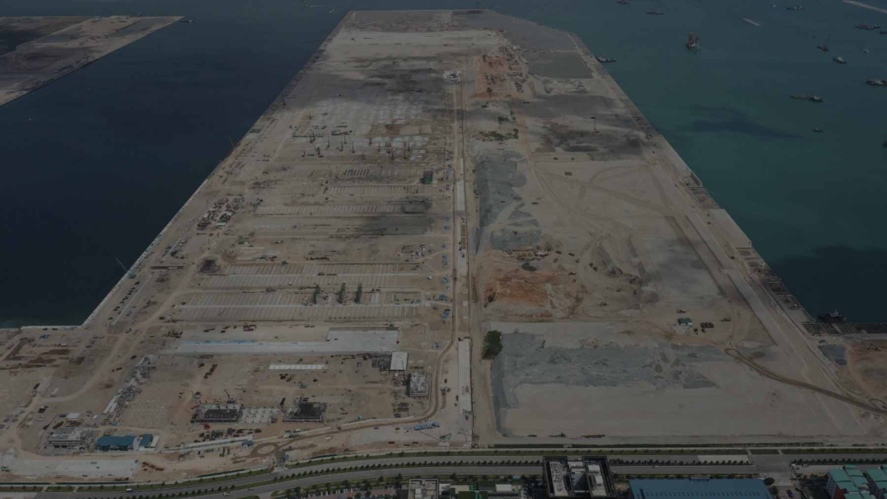 Massive concrete caissons being positioned to form the seawall for the automated Tuas Port development in Singapore, representing advanced port infrastructure and maritime logistics.