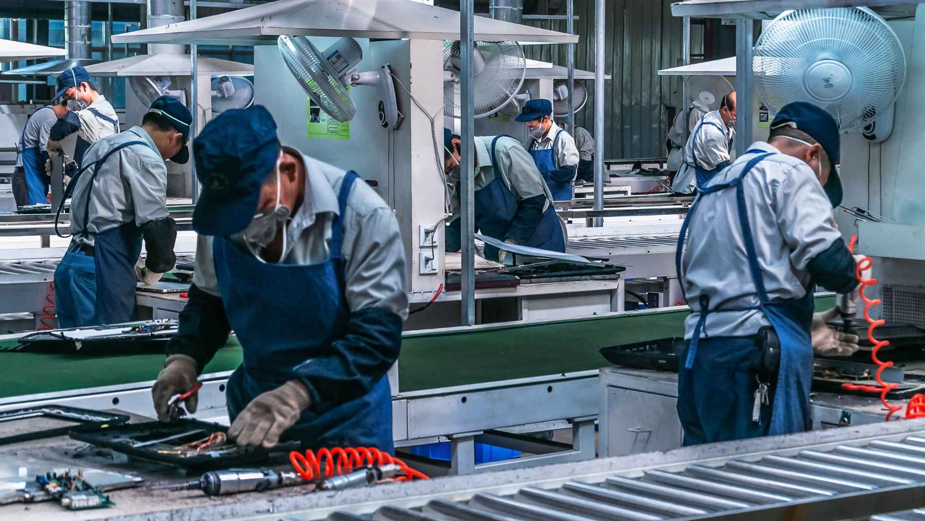 Workers and automated industrial technology operating inside an export manufacturing factory in Tijuana, Mexico.