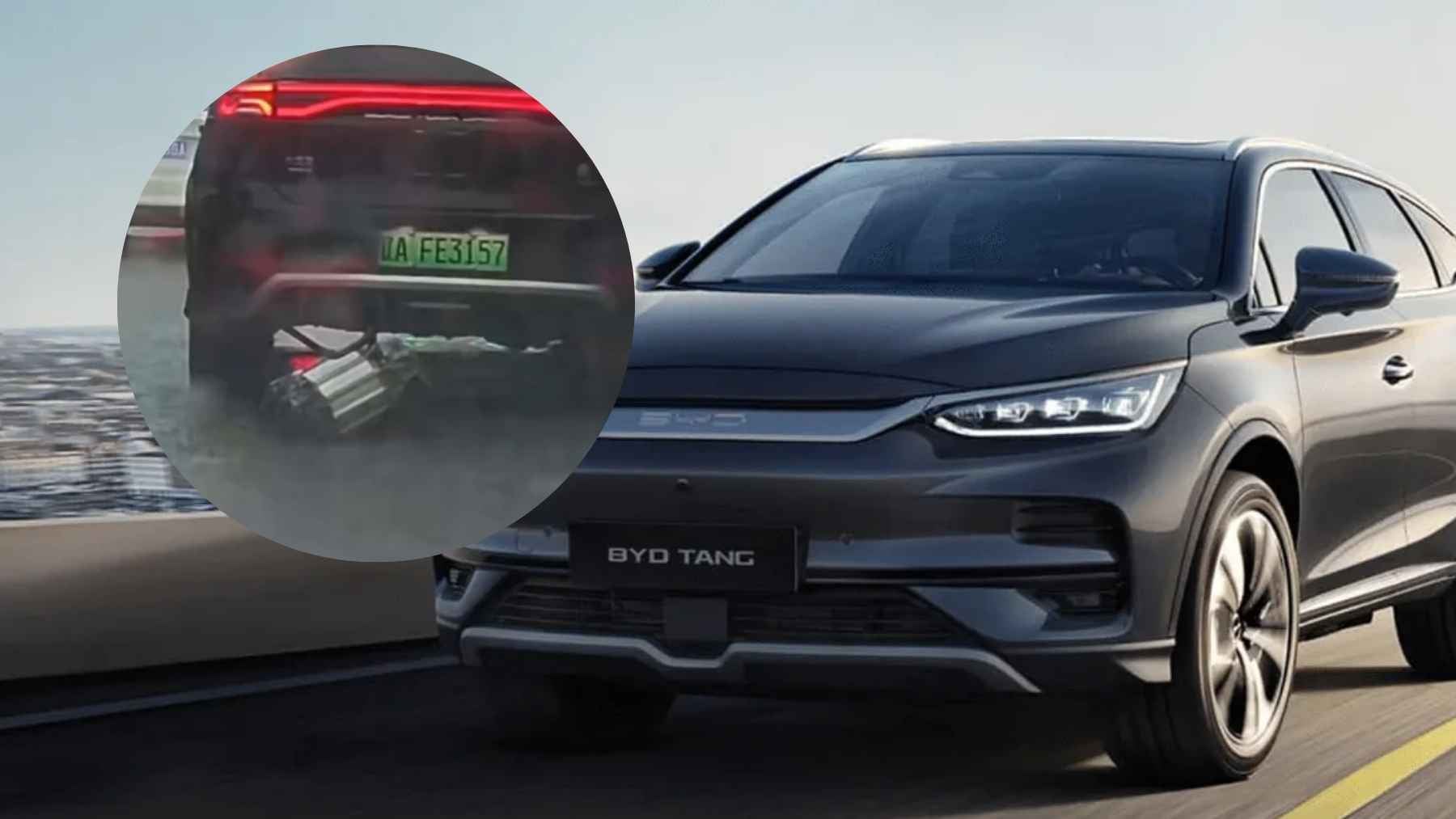 A BYD electric vehicle driving through flooded urban streets with visible underbody damage.