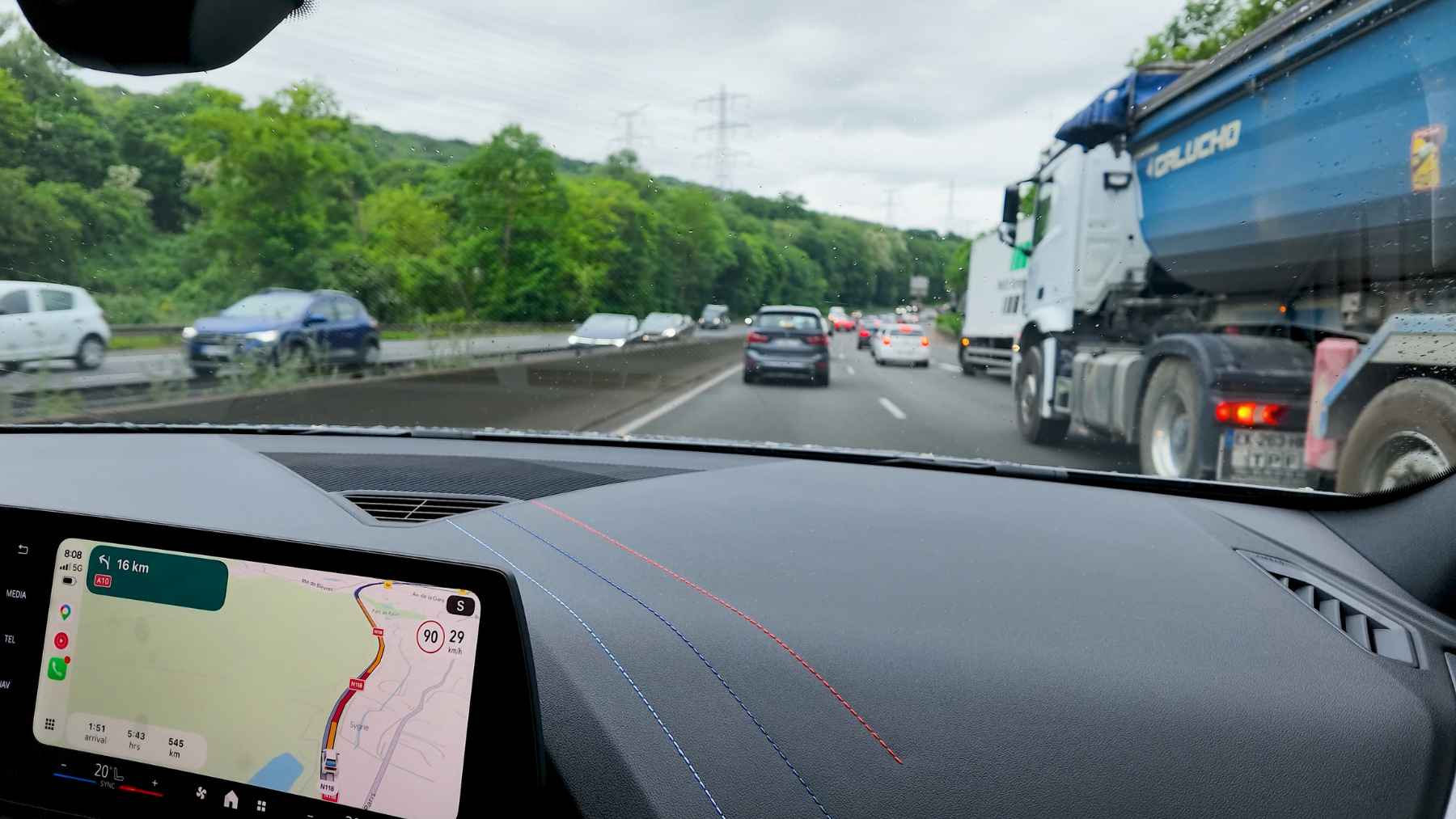 A car dashboard screen displaying navigation and speed limit recognition data next to the steering wheel.