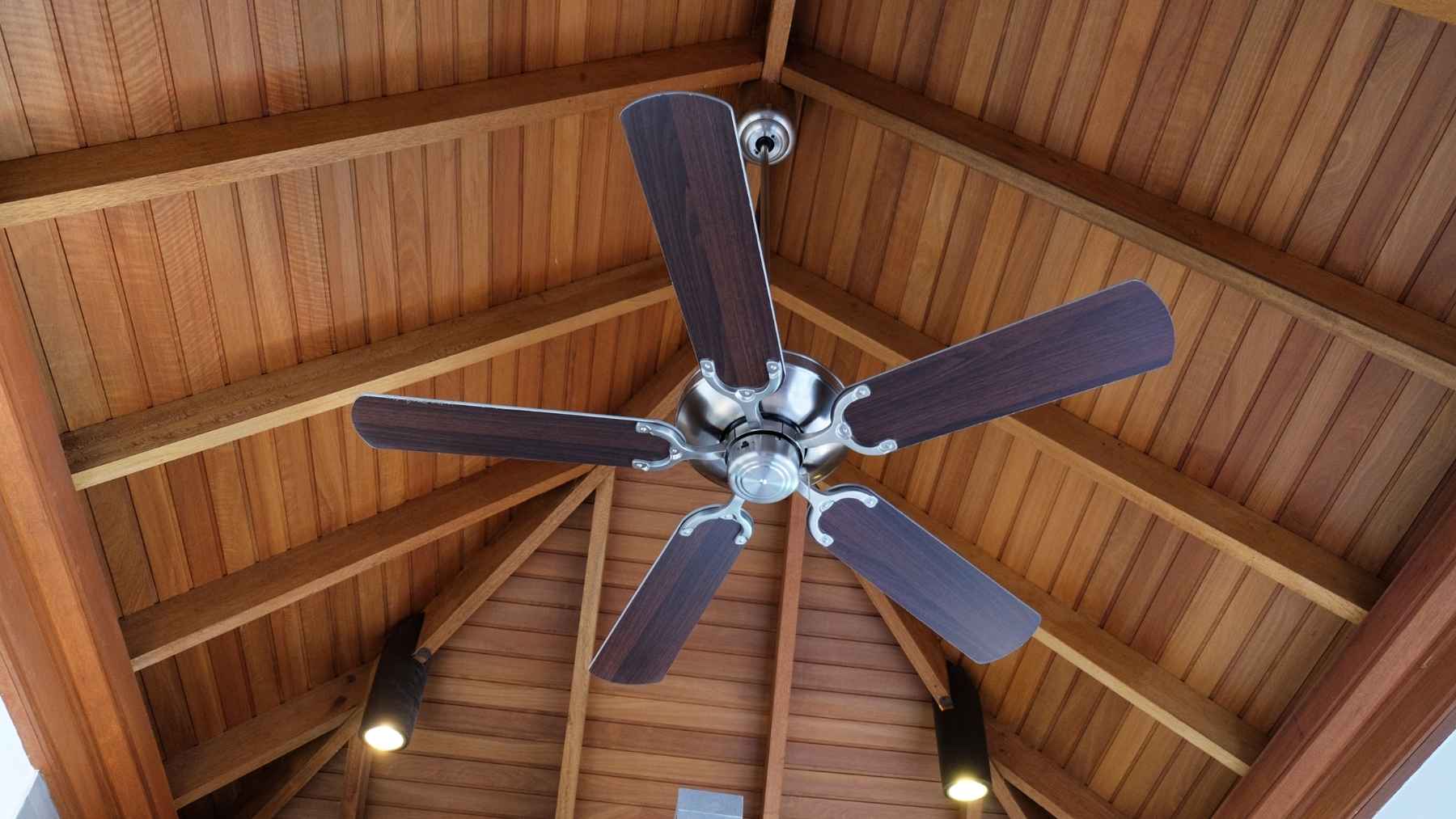 A modern ceiling fan spinning in a bright, comfortable living room with an air-conditioned interior.