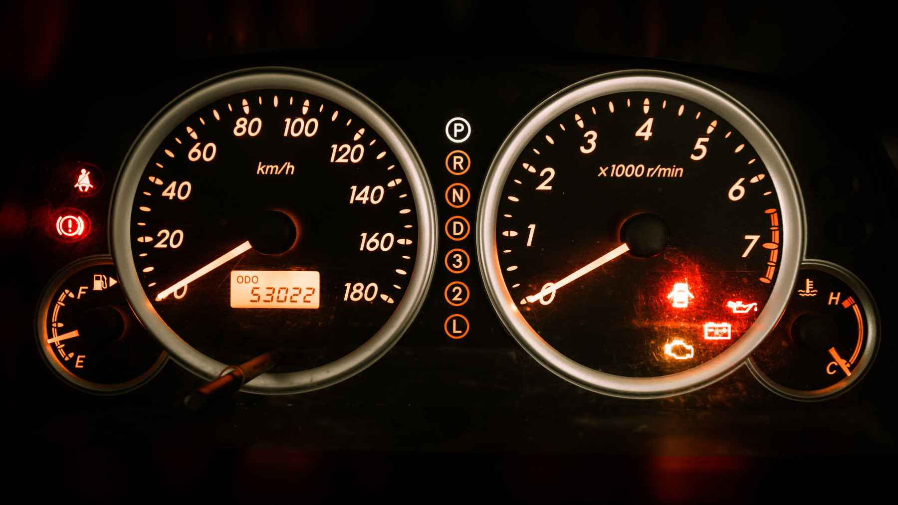 A car dashboard fuel gauge showing the needle resting on the E symbol with a low fuel warning light illuminated.