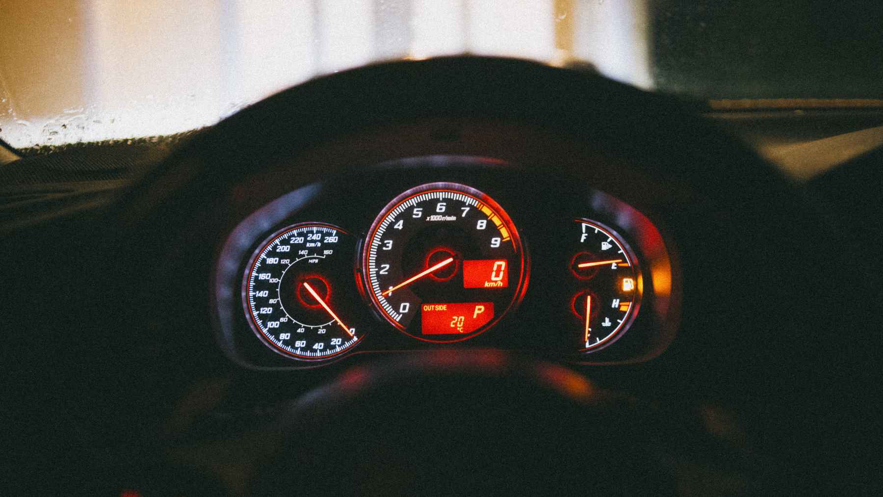 A car dashboard fuel gauge showing the needle resting on the E symbol with a low fuel warning light illuminated.