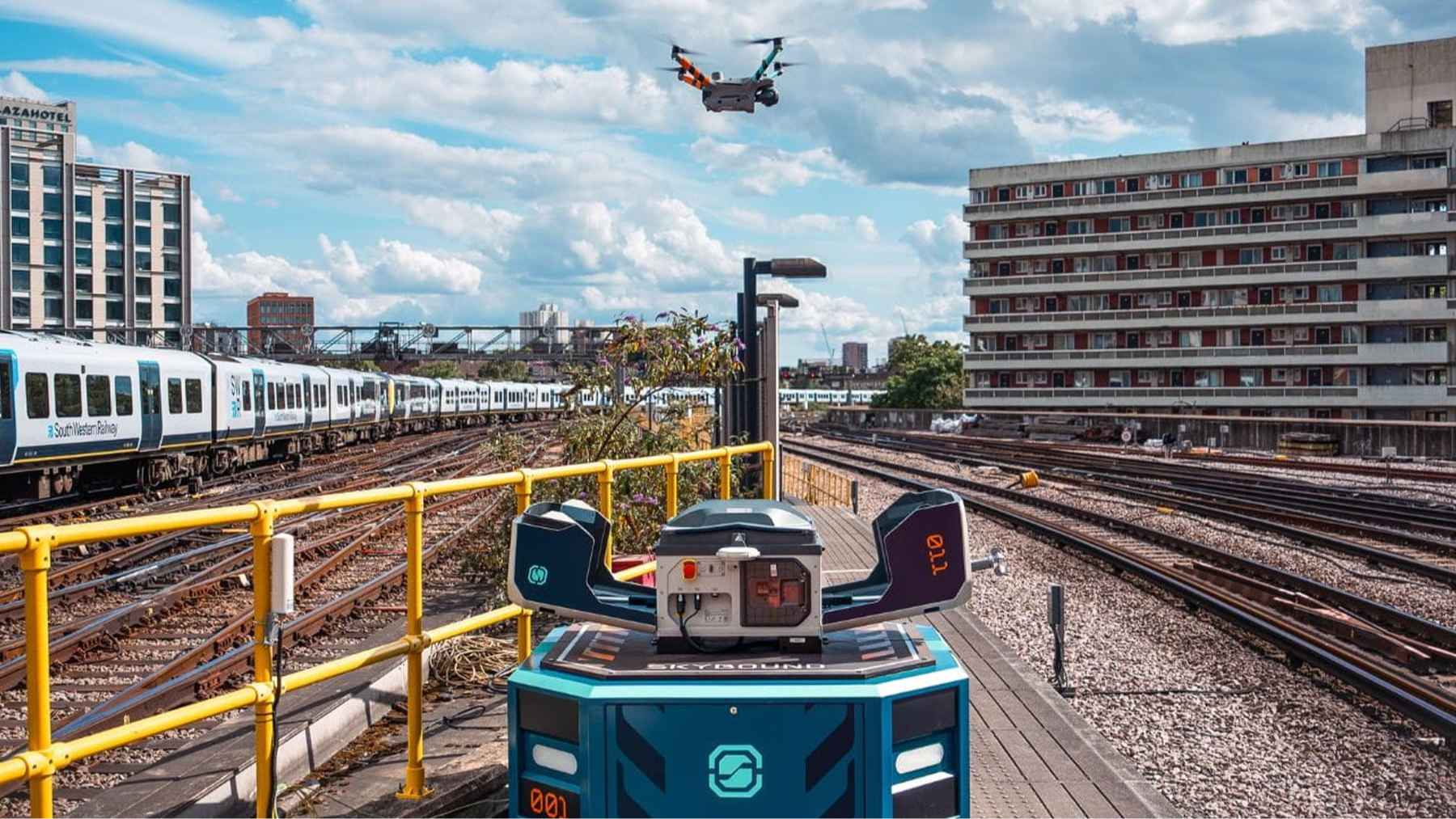 A high-resolution surveillance drone hovering above railway tracks near a busy London transit terminal.