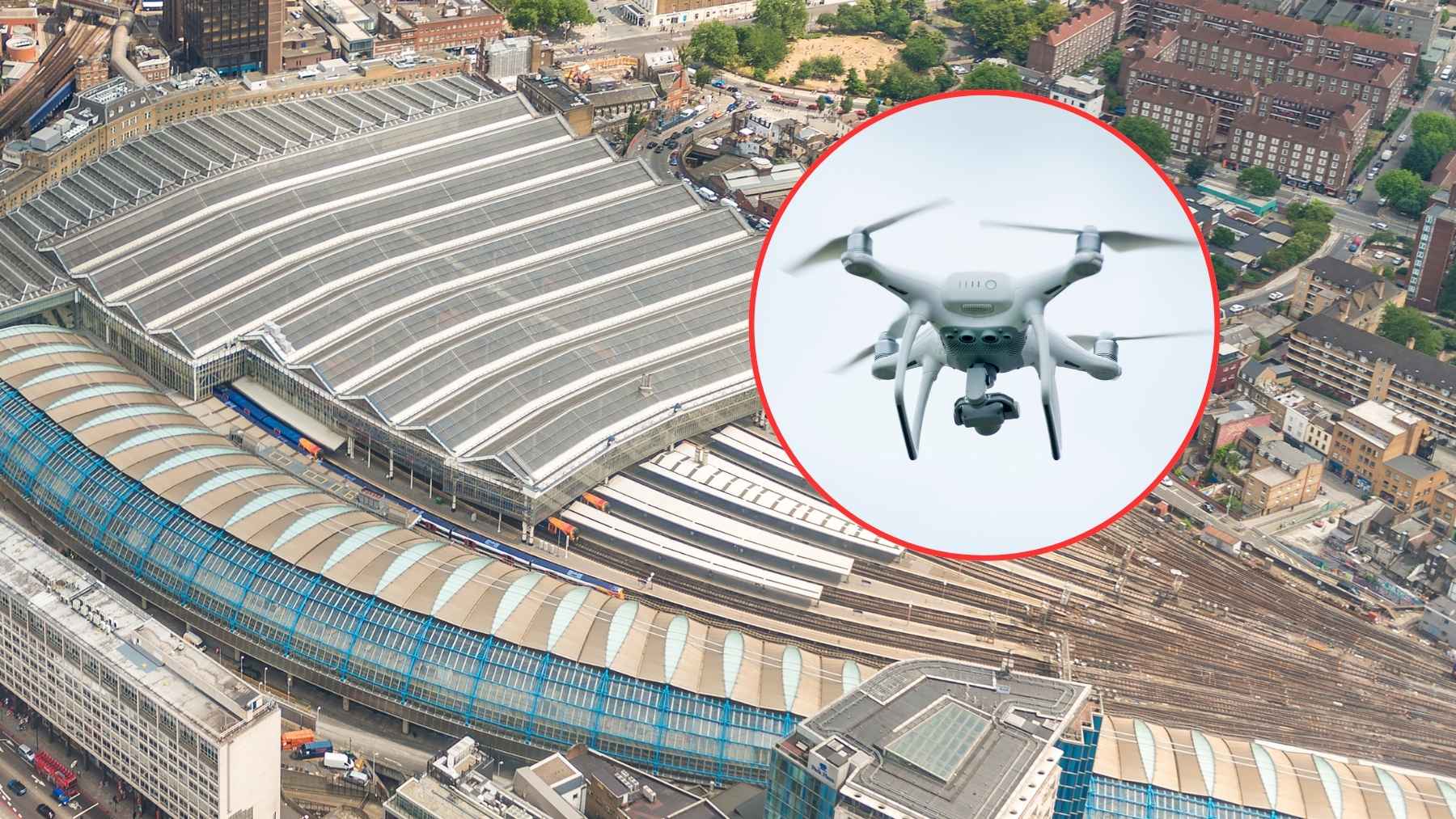 A high-resolution surveillance drone hovering above railway tracks near a busy London transit terminal.