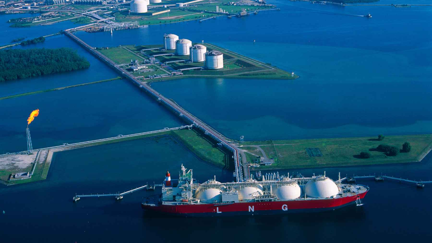 LNG carrier ship docked at an industrial port terminal, representing liquefied natural gas trade and energy supply security.