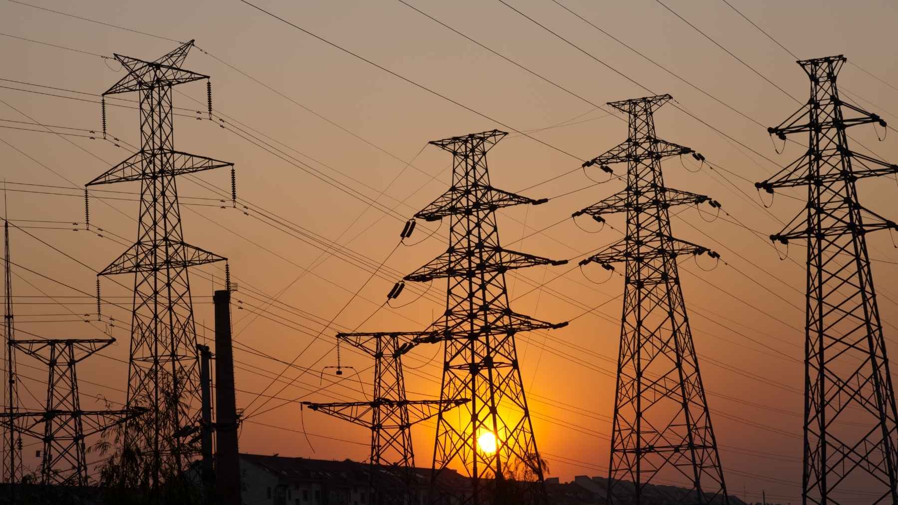 Power transmission towers and electric grid lines operating under intense summer heat.