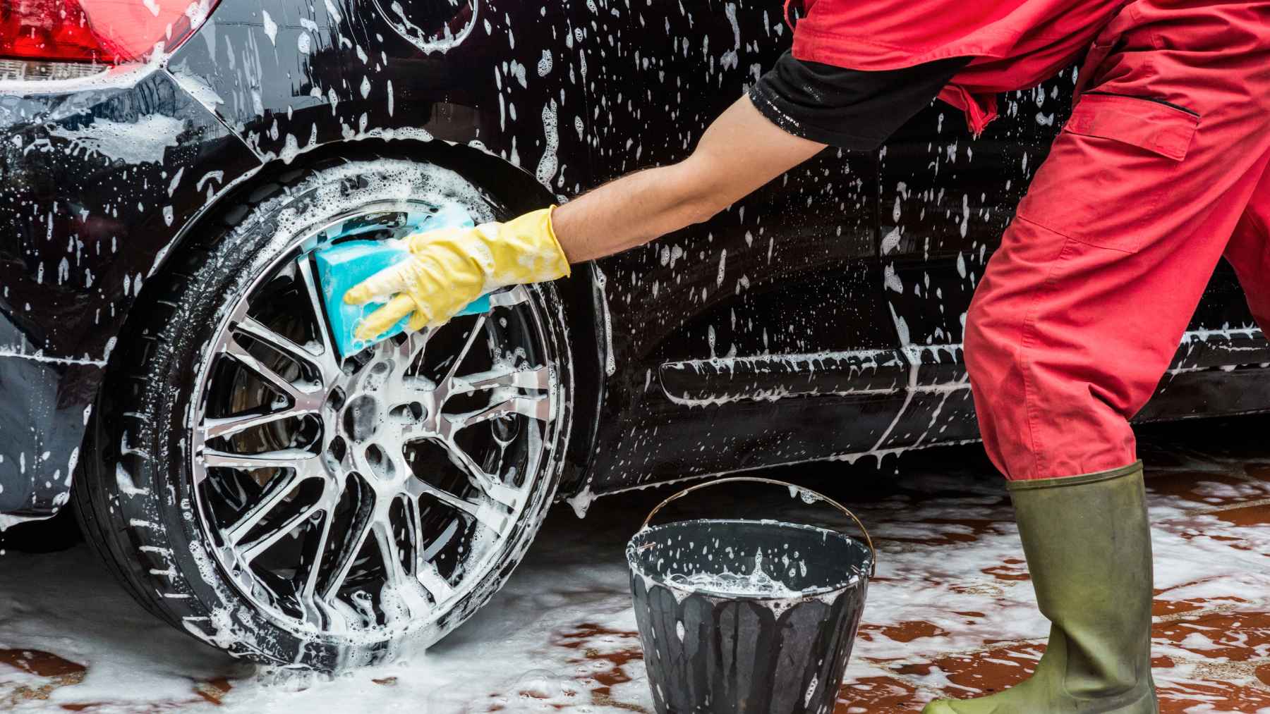 A professional detailer meticulously polishing and cleaning a luxury vehicle in a high-end car care shop.